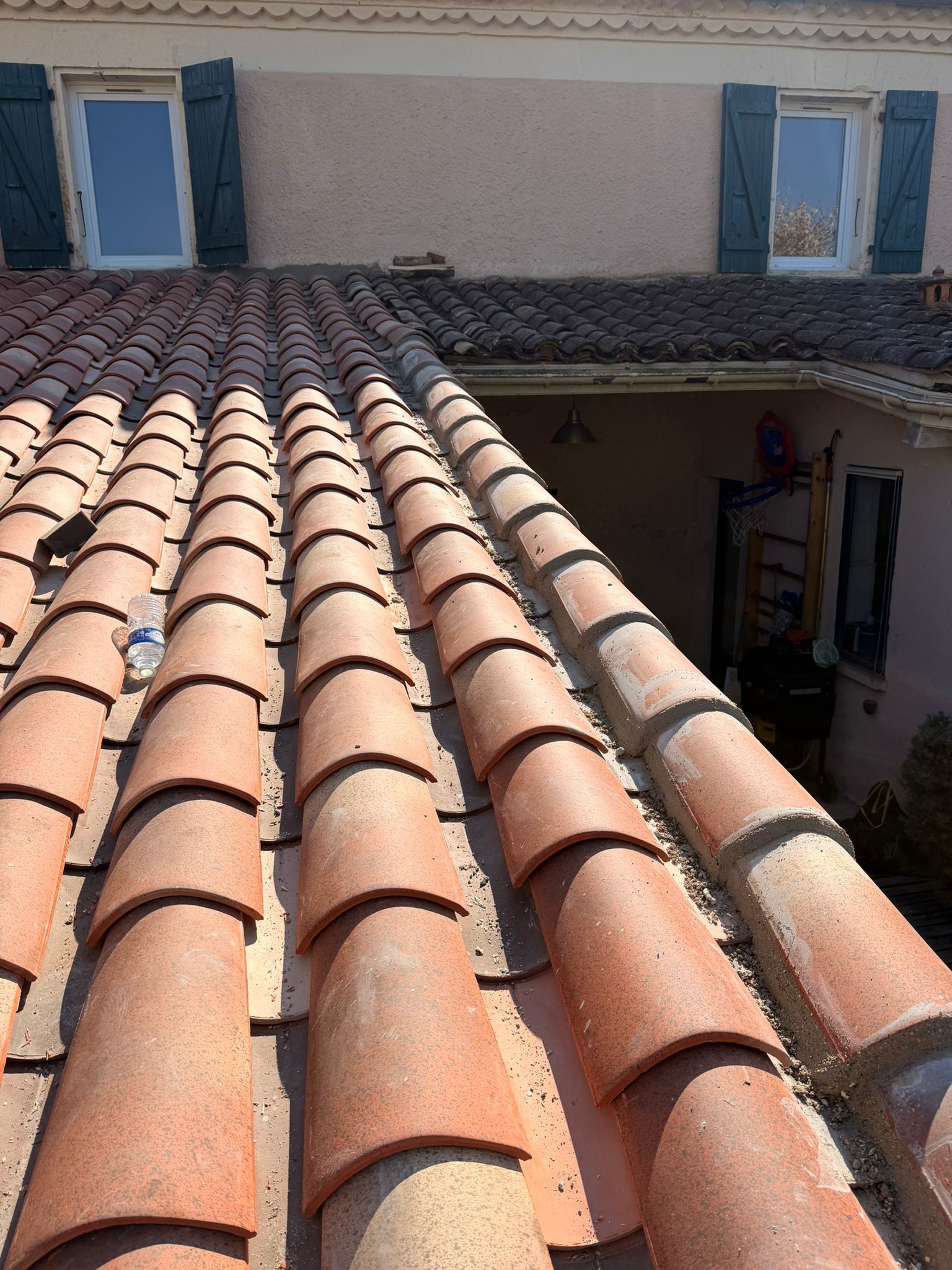 Couvreur nettoyant une gouttière en zinc remplie de feuilles mortes sur une maison à Saint-Girons