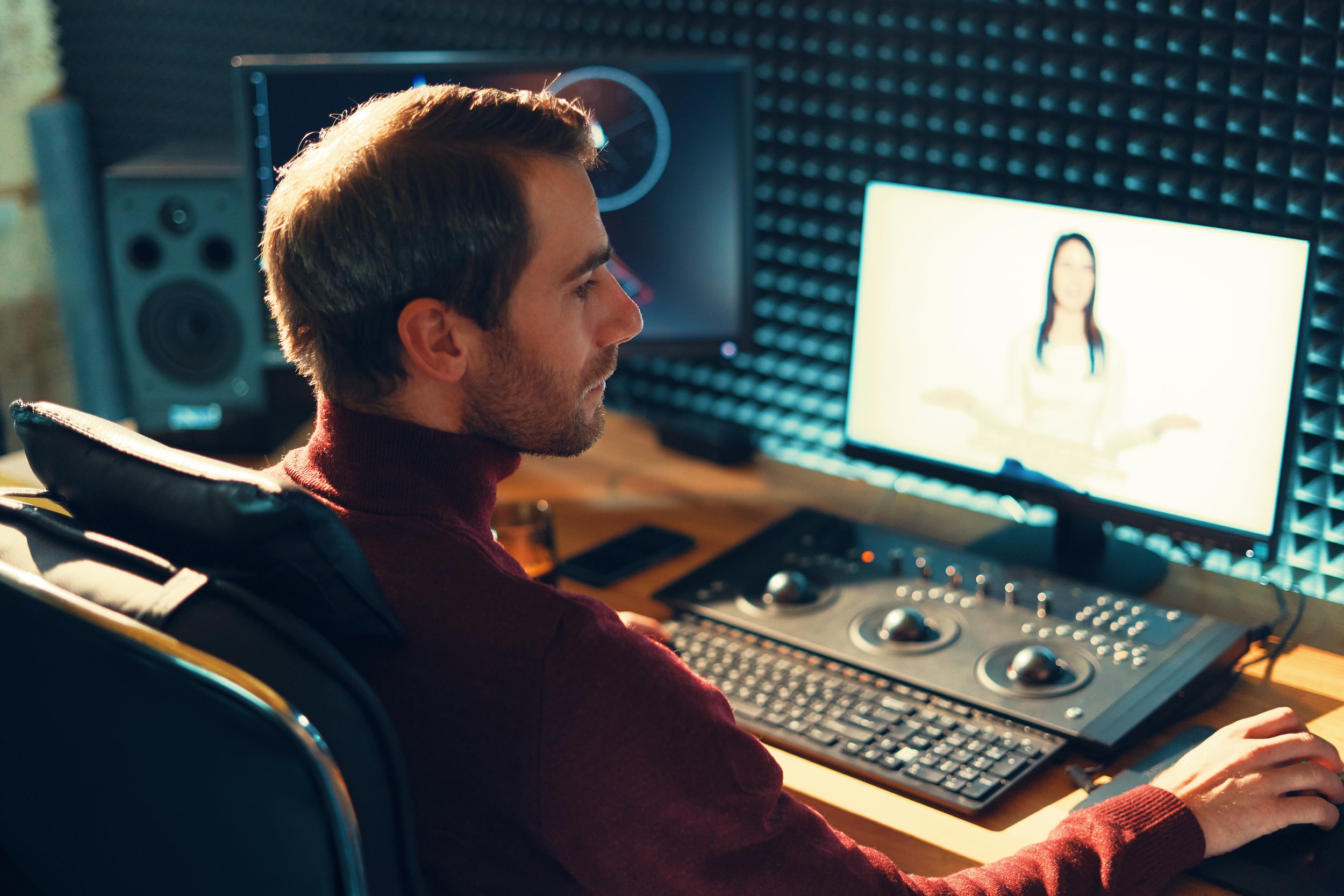 An editor seated at a workstation with an interview on the monitor and audio equipment beside it.