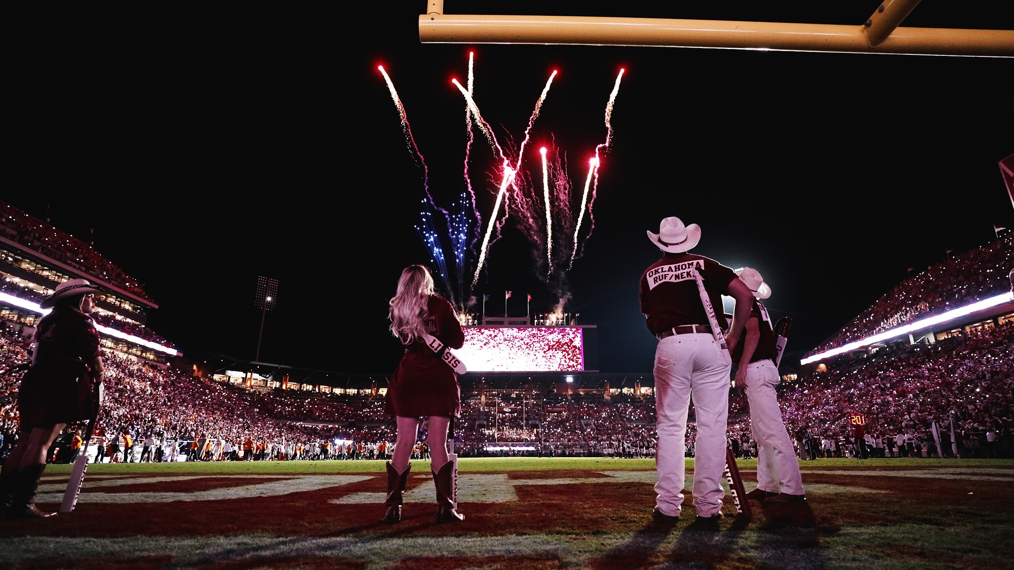 A stadium lit by fireworks during a post-game celebration with cowboy-hat-wearing personnel on the field.