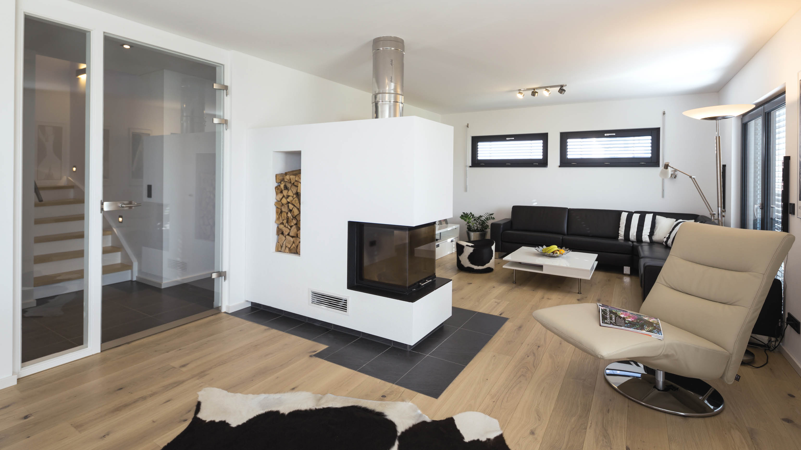 Modernes Wohnzimmer mit weißem Kamin, Ledercouch, einem beigen Sessel und Holzboden.