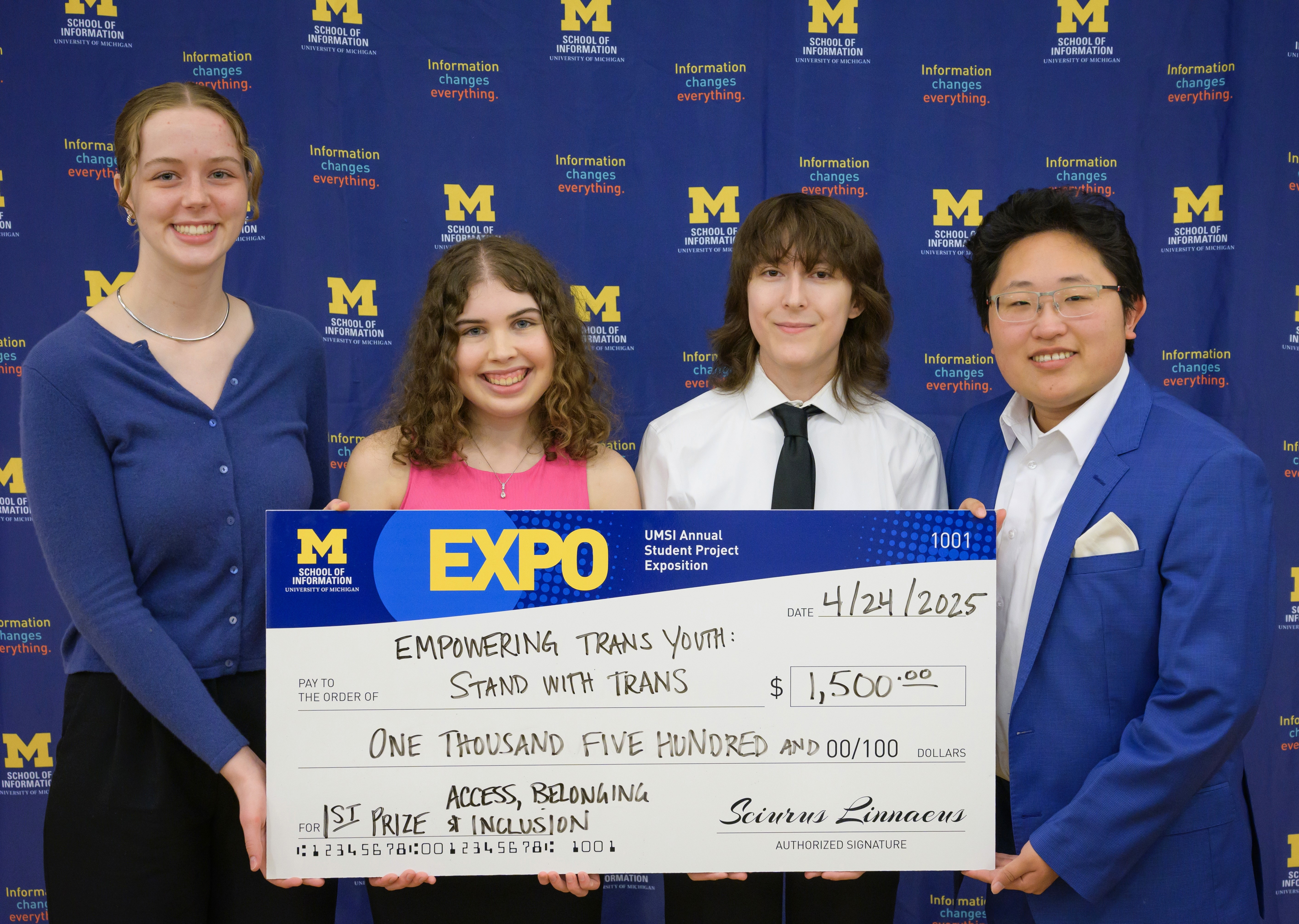 Four people holding award check in front of University of Michigan School of Information branded backdrop