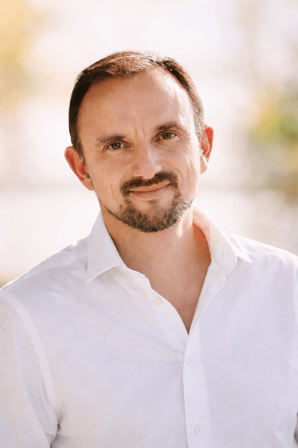 A smiling man with glasses, curly hair, wearing a maroon hoodie, poses against a dark background.