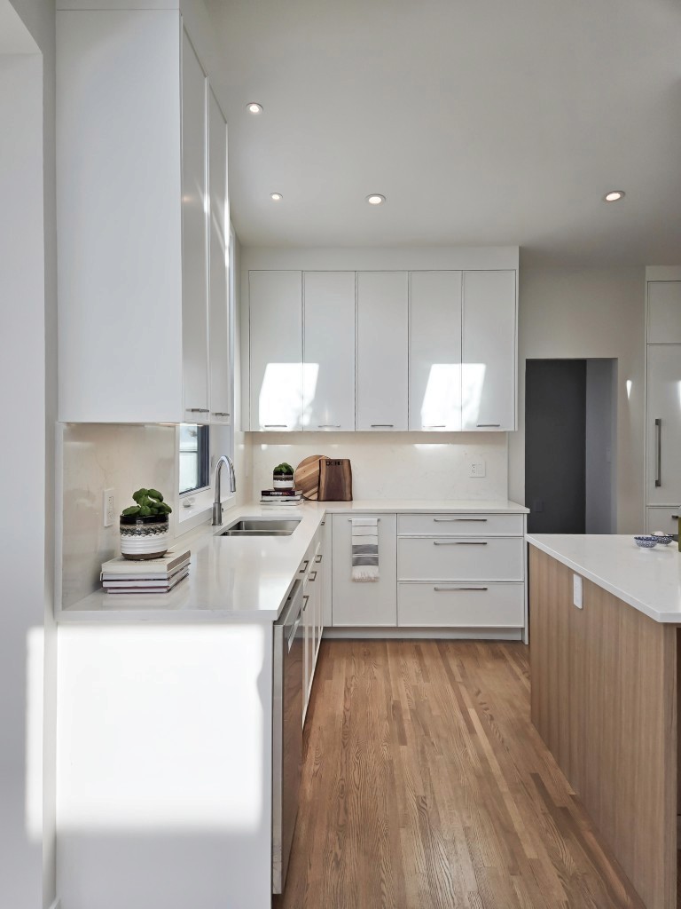 Image of Modern kitchen design with white cabinets, countertops, and hardwood floors by KHD Homes.