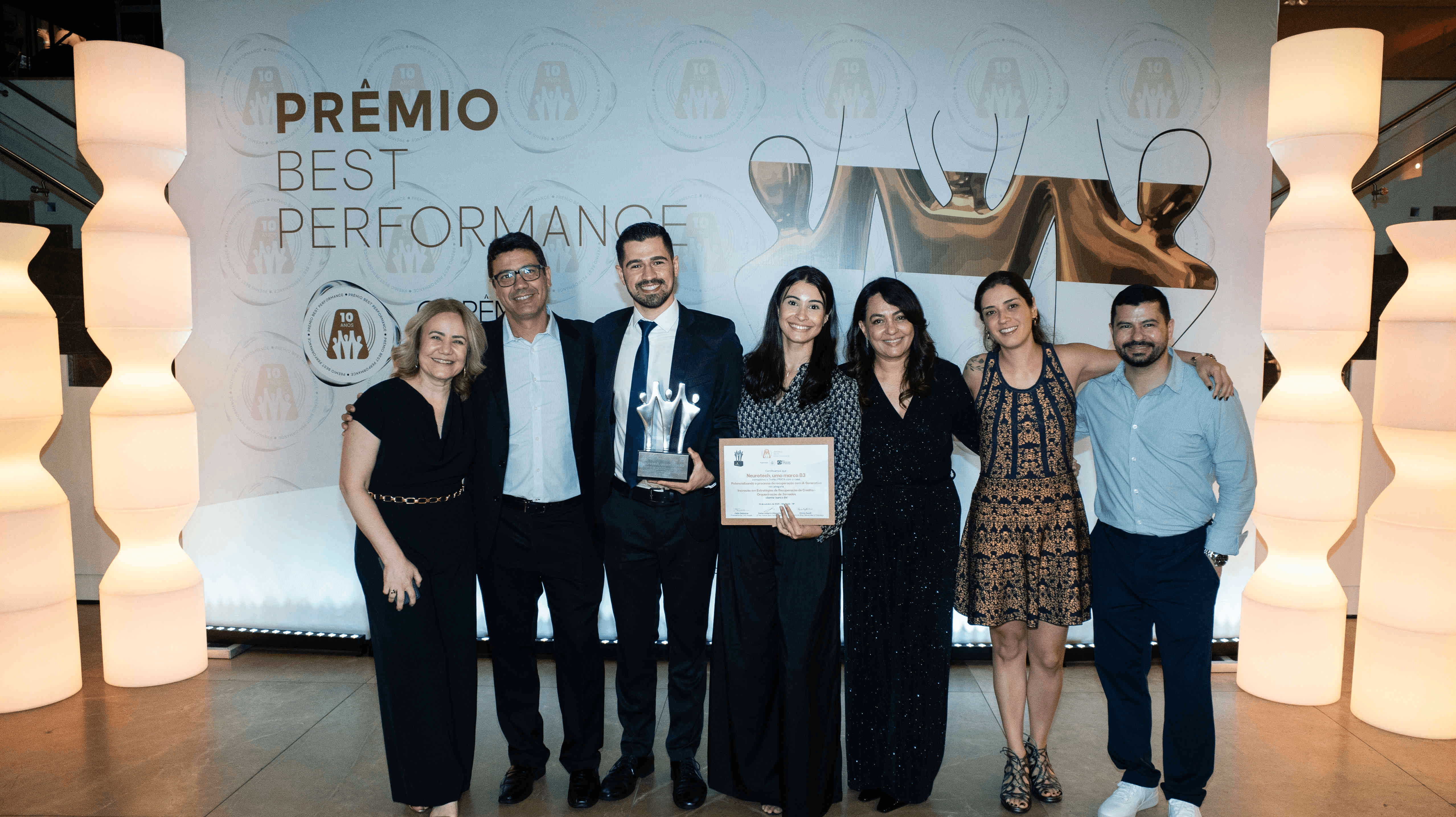 Executivos da Neurotech, uma marca B3 posando com troféu prata e certificado no palco do Prêmio Best Performance 2025