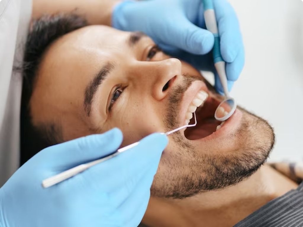 A man sitting in a dentist's chair while the dentist examines his teeth.