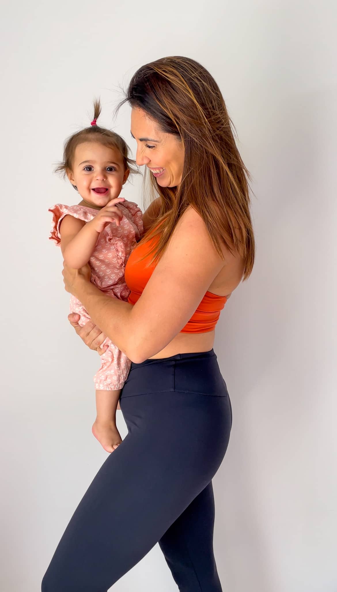 Jeune maman souriante portant sa fille, représentant l'énergie et la confiance retrouvées grâce au mouvement au quotidien.