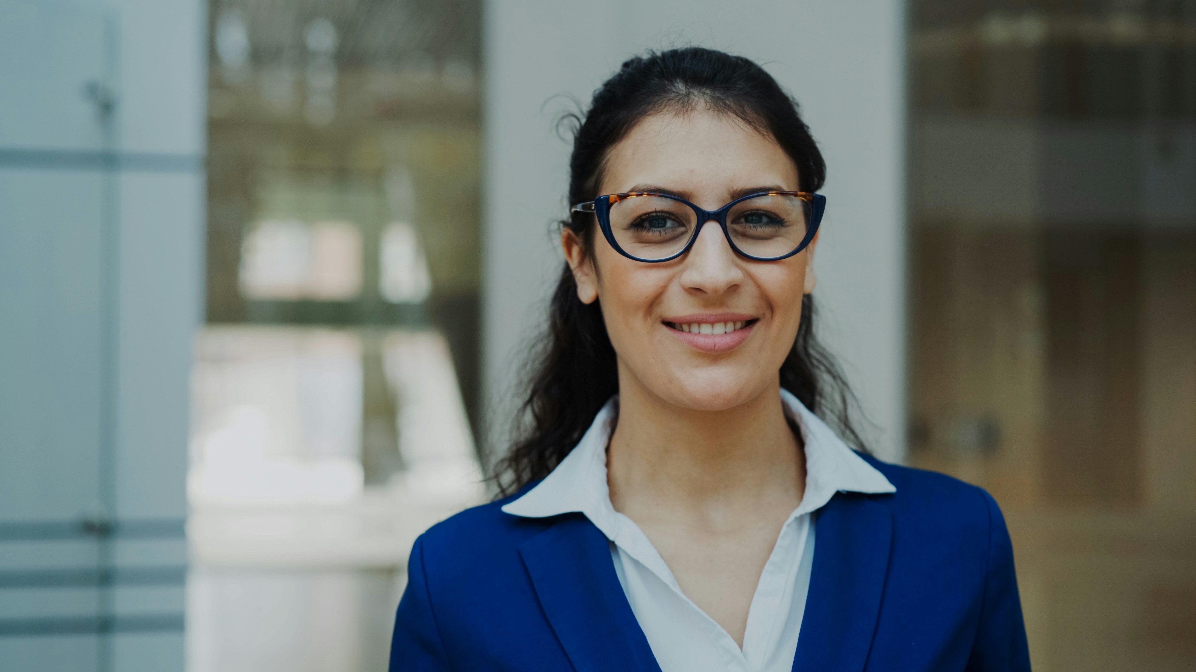 A smiling woman wearing glasses and a blue suit.
