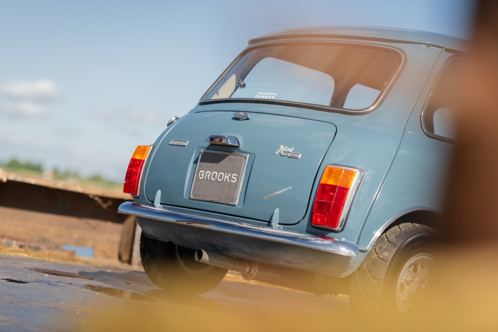 A vintage blue car parked on a sandy beach, with a scenic view and blue sky in the background.