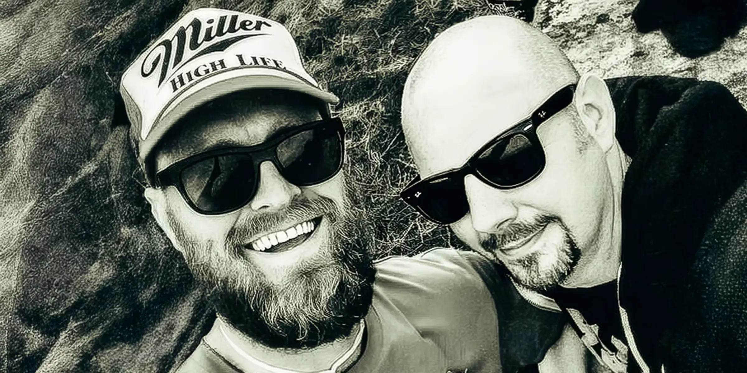Black-and-white photo of two men smiling outdoors at a music festival, capturing a relaxed, candid moment of friendship and collaboration.