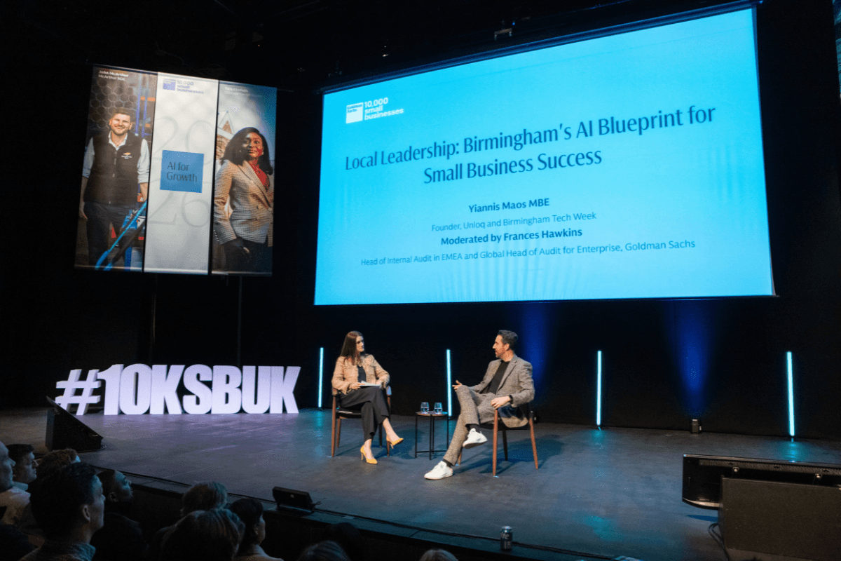Unloq CEO, Yiannis Maos being interviewed by Frances Hawkins, Head of Internal Audit at Goldman Sachs about artificial intelligence and how SMEs can successfully adopt AI. The conversation is happening on stage with a large projector in the background showing their names.