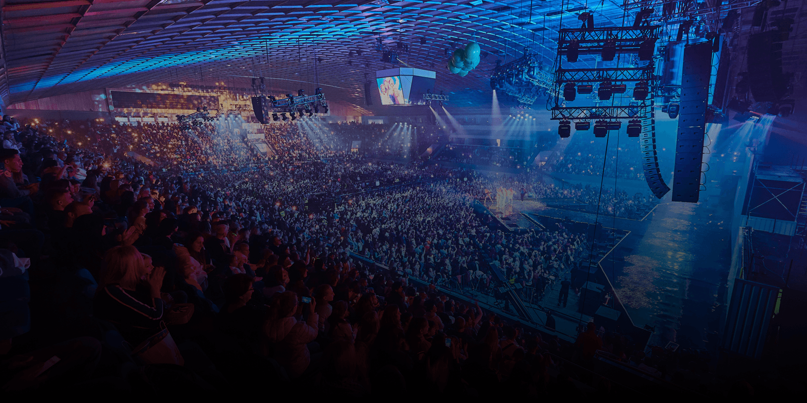 Audience in a large concert arena with stage lighting