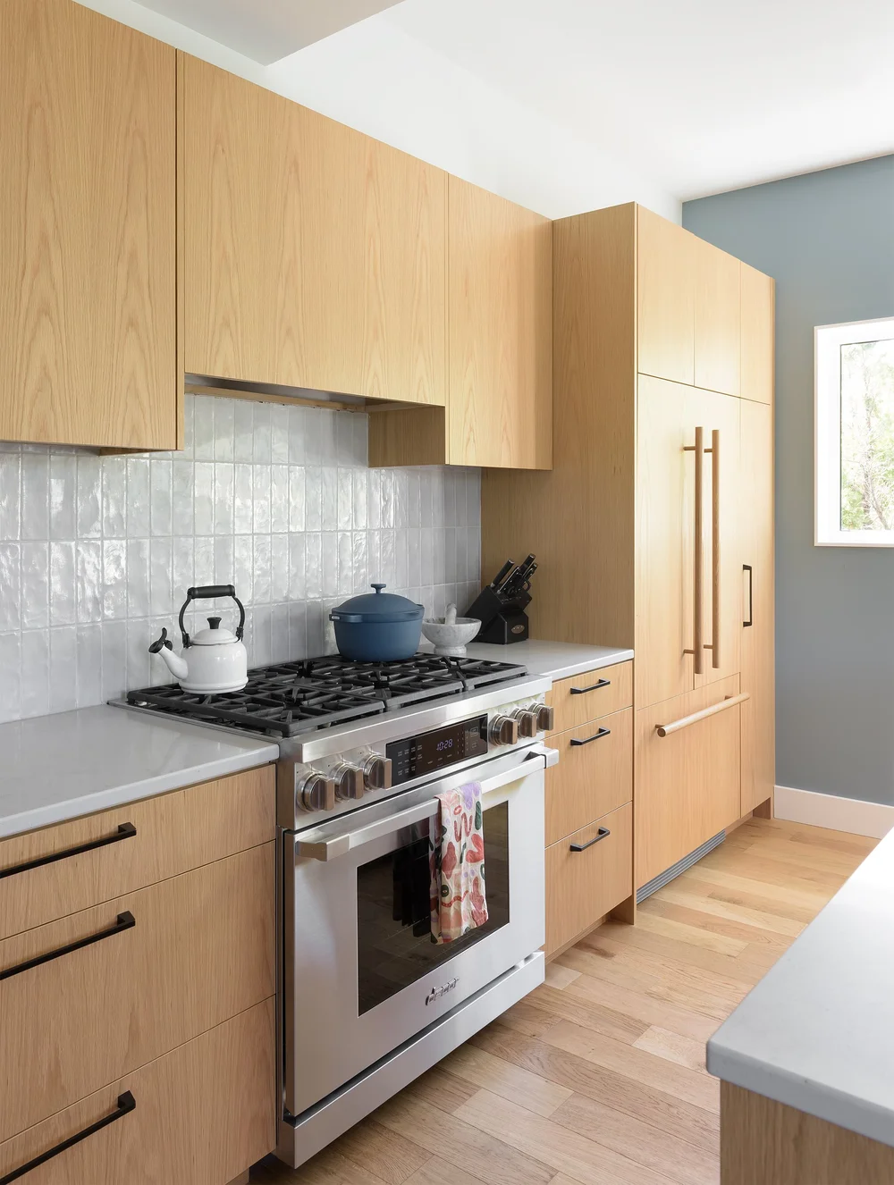 Modern two-story home with large glass windows, warmly lit interiors, and a balcony. Surrounded by trees and a manicured lawn at dusk. Cozy ambiance.