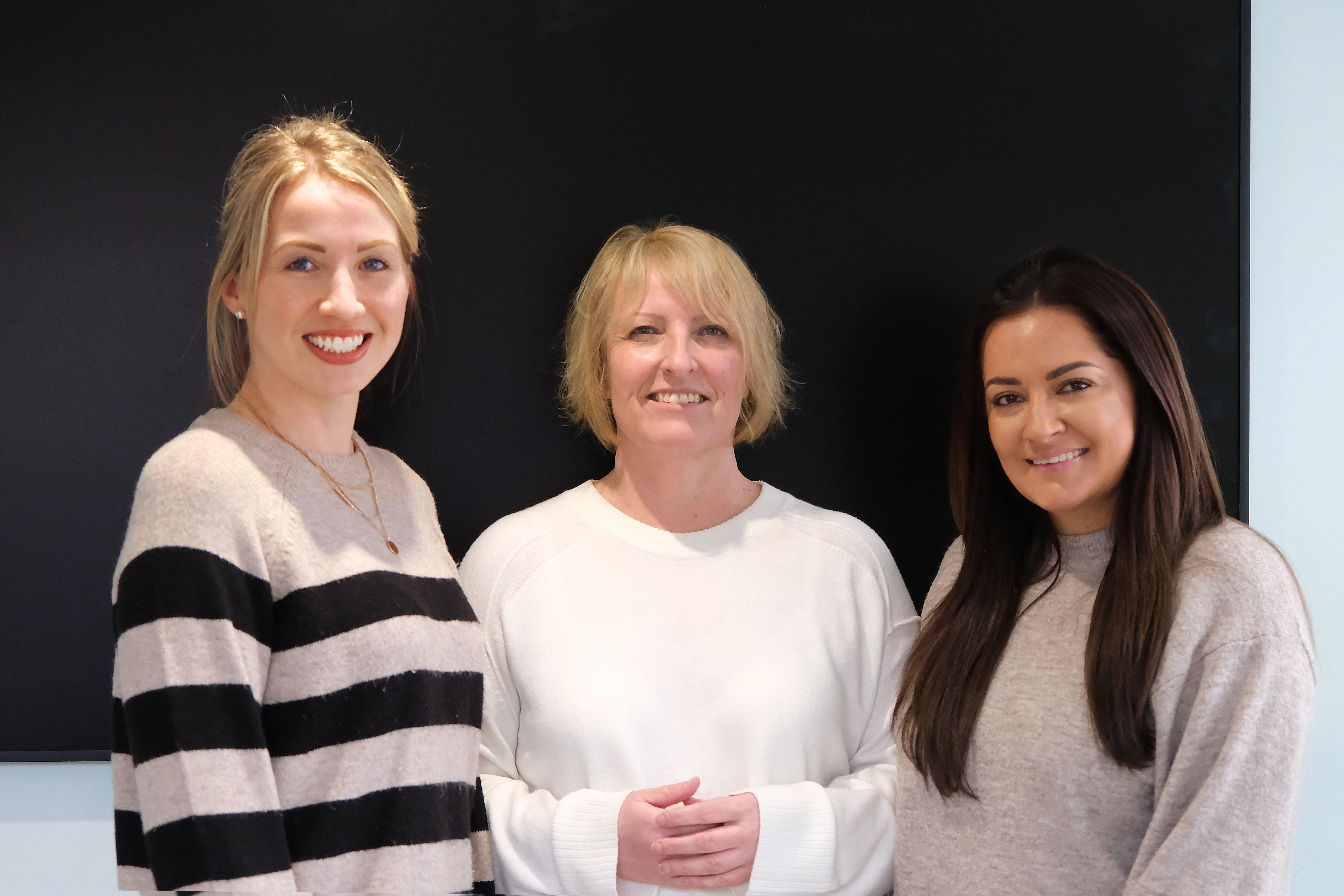 A large group photo of diverse team members gathered in an industrial-style space with arched ceiling.