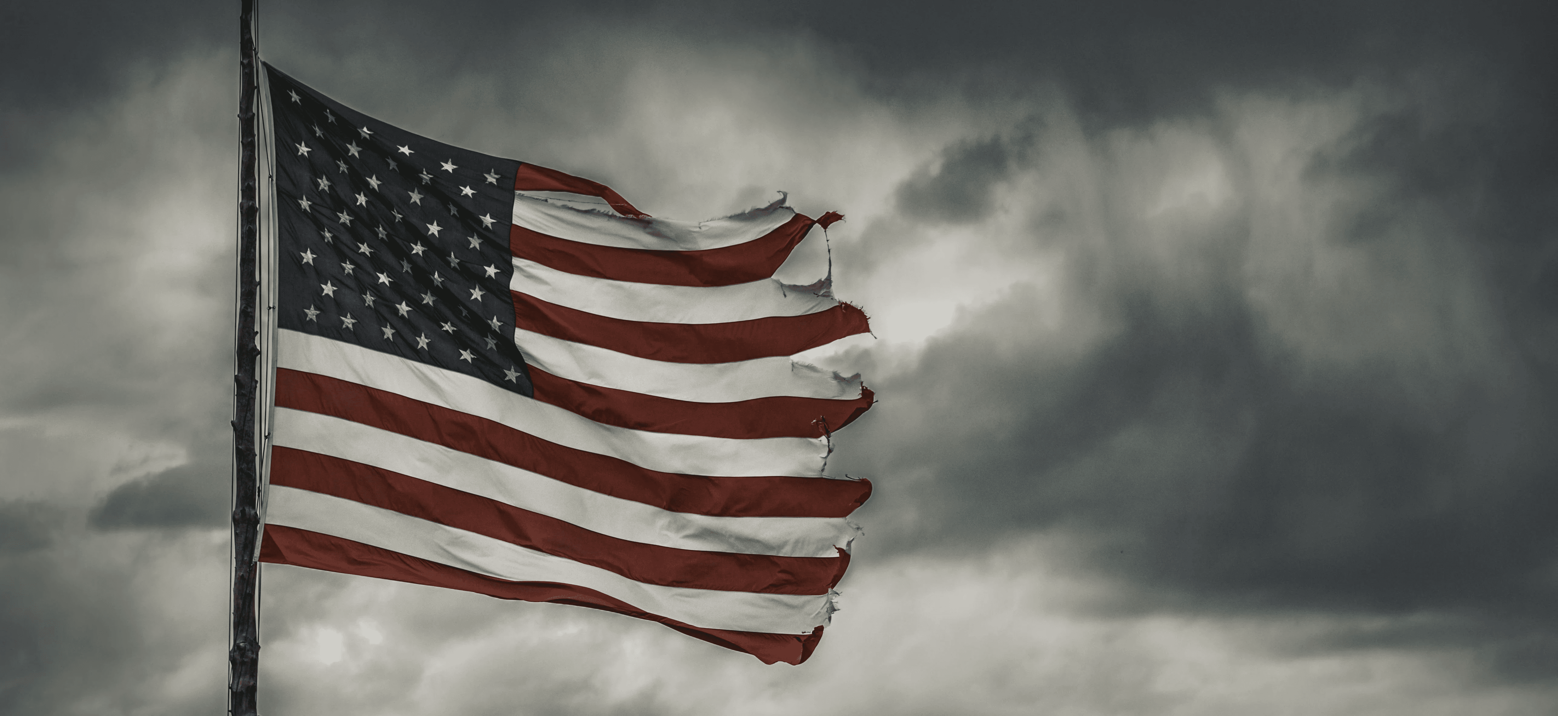 a large american flag flying in a cloudy sky