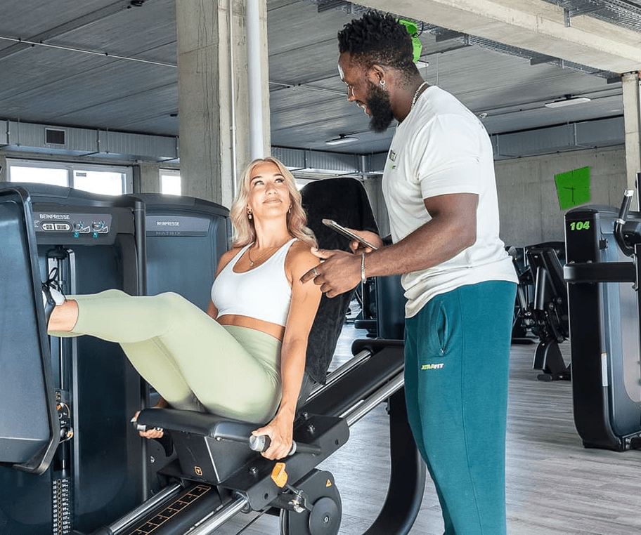 Ein XTRAFIT-Trainer gibt einer Frau Anweisungen an einem Trainingsgerät.