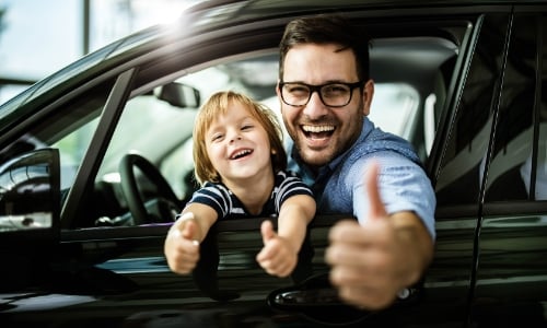 Father and child in a car making the OK sign, representing vehicle insurance coverage from We Insure Downtown Miami.