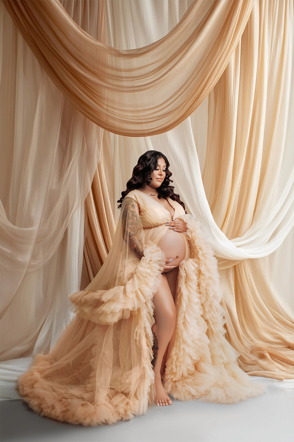 Expecting mother posing in a fluffy gown surrounded by warm light — elegant pregnancy photo.