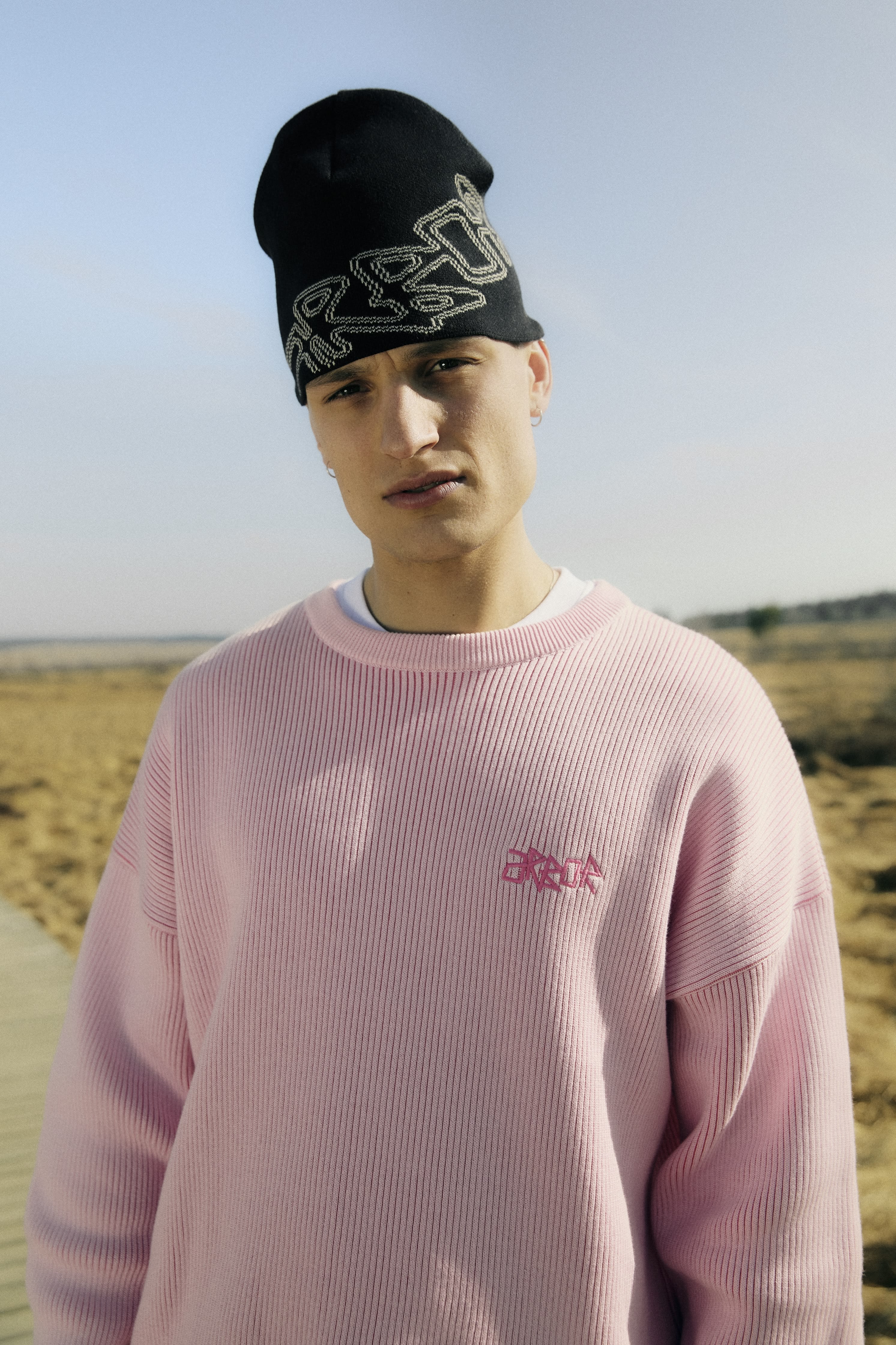 Plan américain d'un mannequin portant un bonnet en maille noire et un pull rose dans le lookbook Arbor Antwerpen