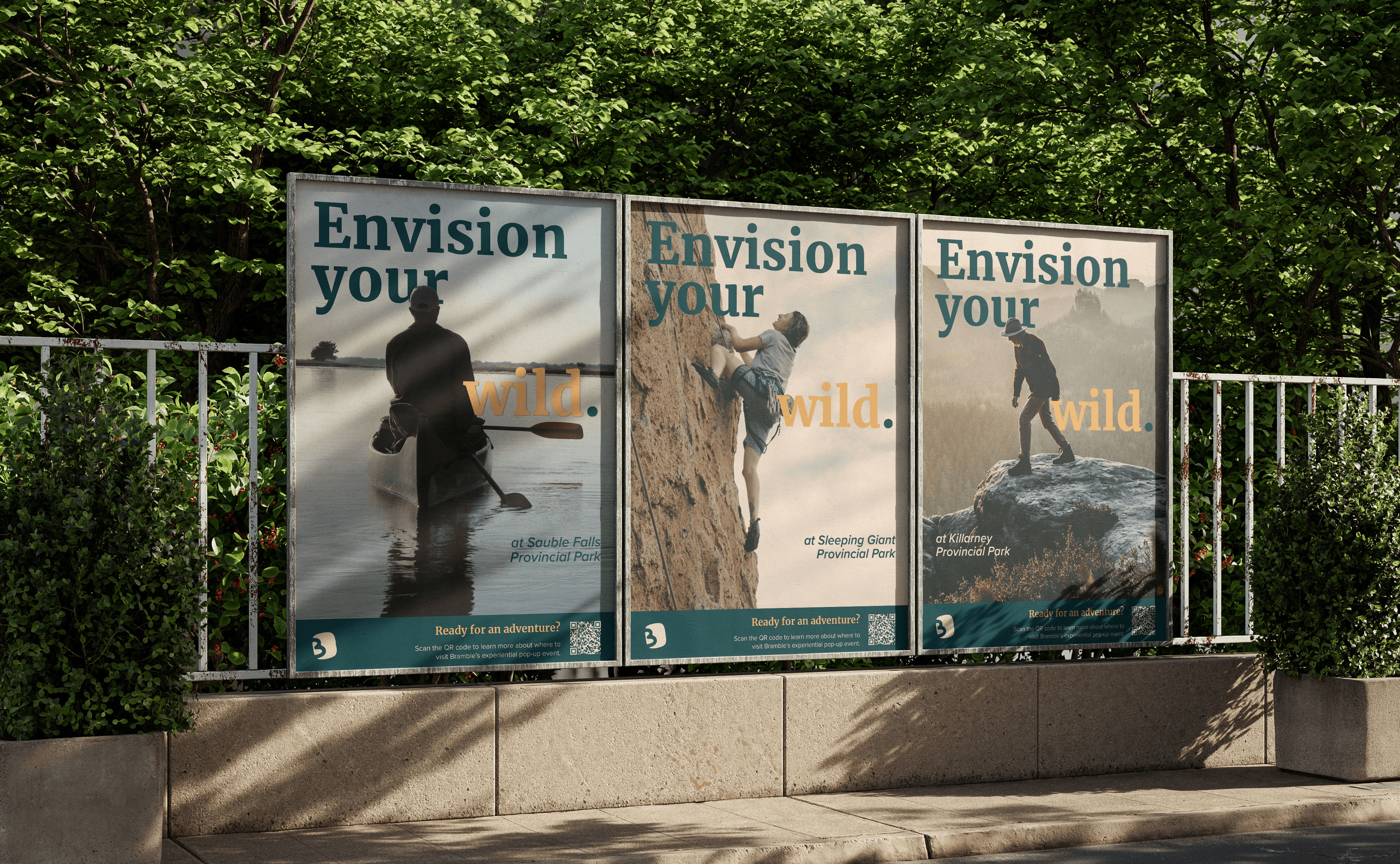 Gemini said Three outdoor advertising posters for the brand Bramble are displayed in a row on a metal fence along a sidewalk, set against a backdrop of lush green trees. Each poster features a large, atmospheric photograph of an outdoor activity—canoeing, rock climbing, and hiking—accompanied by the bold teal and orange headline "Envision your wild". The posters specify different locations such as Sauble Falls, Sleeping Giant, and Killarney Provincial Parks, and include a dark teal footer with the Bramble logo, a QR code, and the call to action, "Ready for an adventure?".