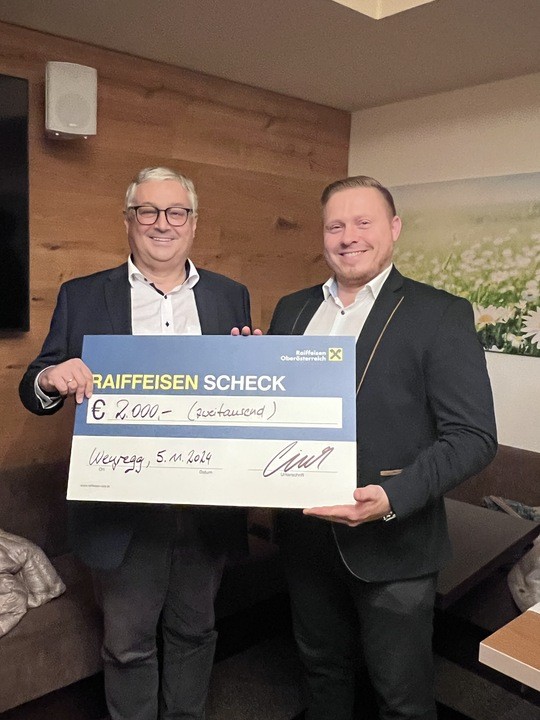 Der Clubspräsident übergibt einen Spendencheck an einem Vertreter der Raiffeisenbank.