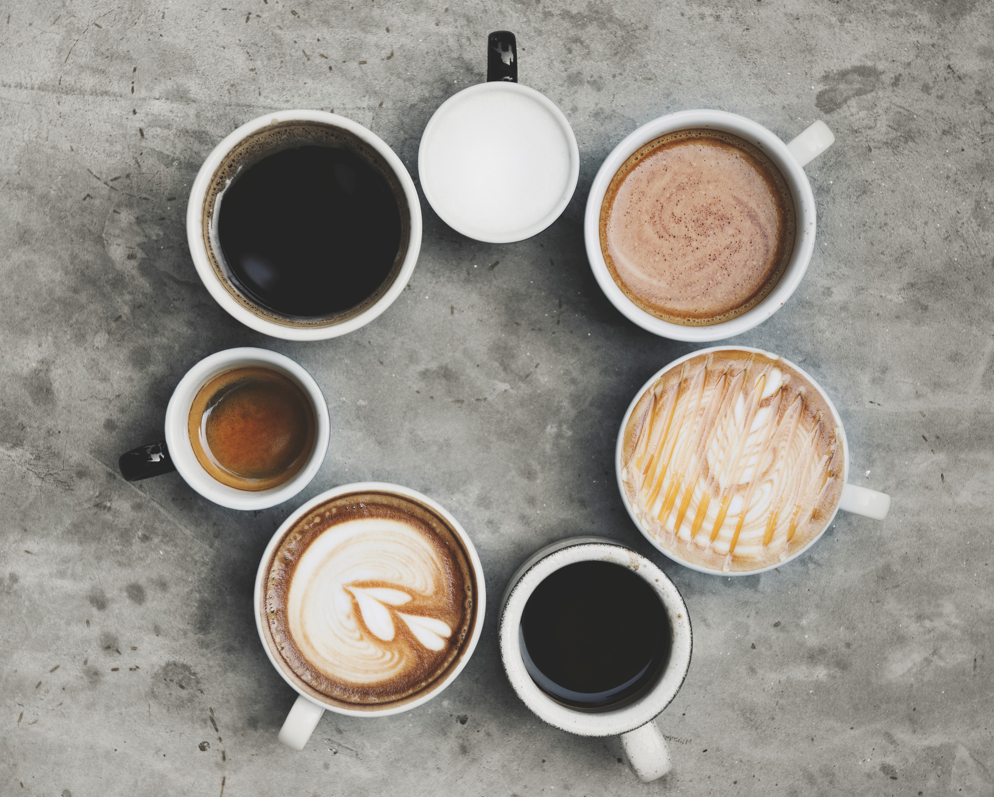 Aerial view of seven cups, each filled with a different type of coffee beverage