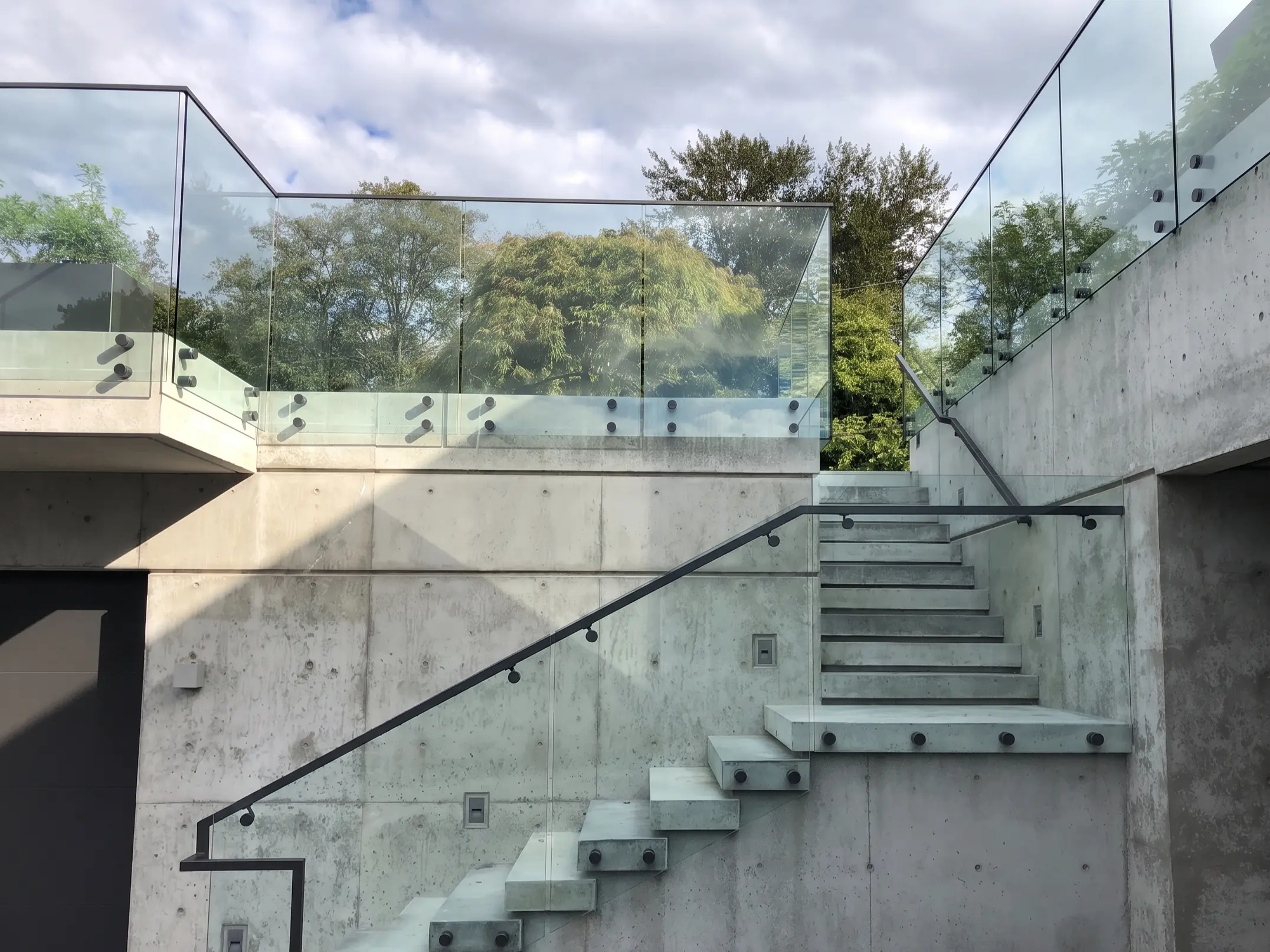 Exterior concrete staircase with glass railings descending a sloped hillside lot on Vancouver Island