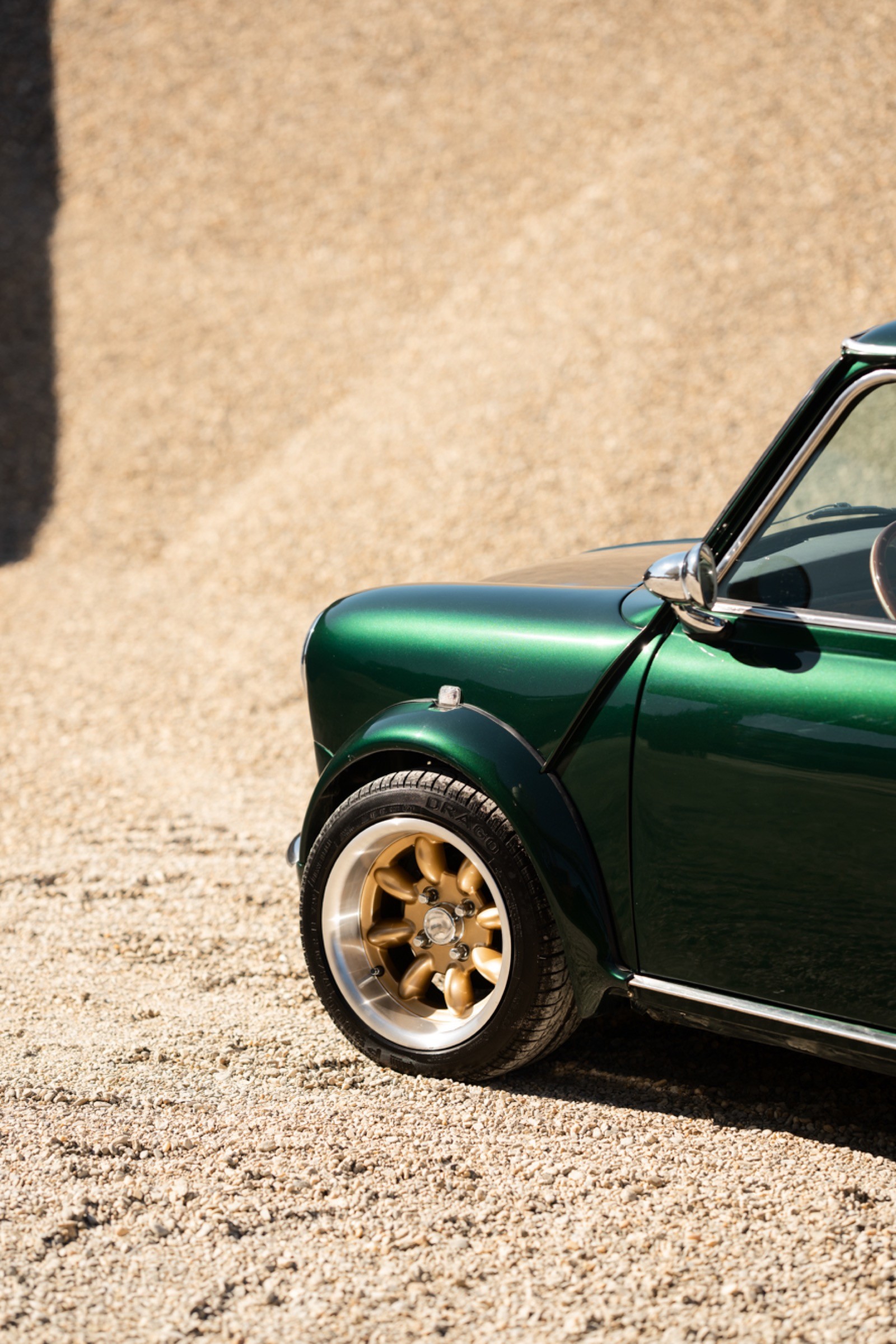 A small, green and black vehicle parked on a sandy surface, with a warm sunset lighting the scene.