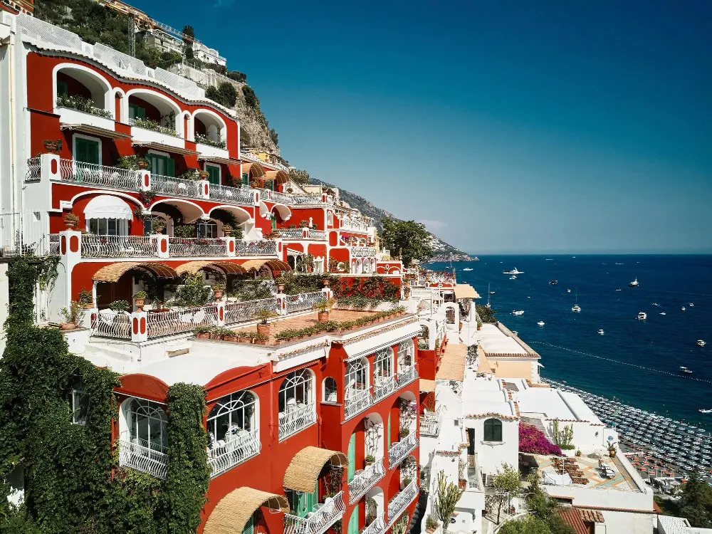 A hotel's red-and-white facade with balconies above Positano and the sea.
