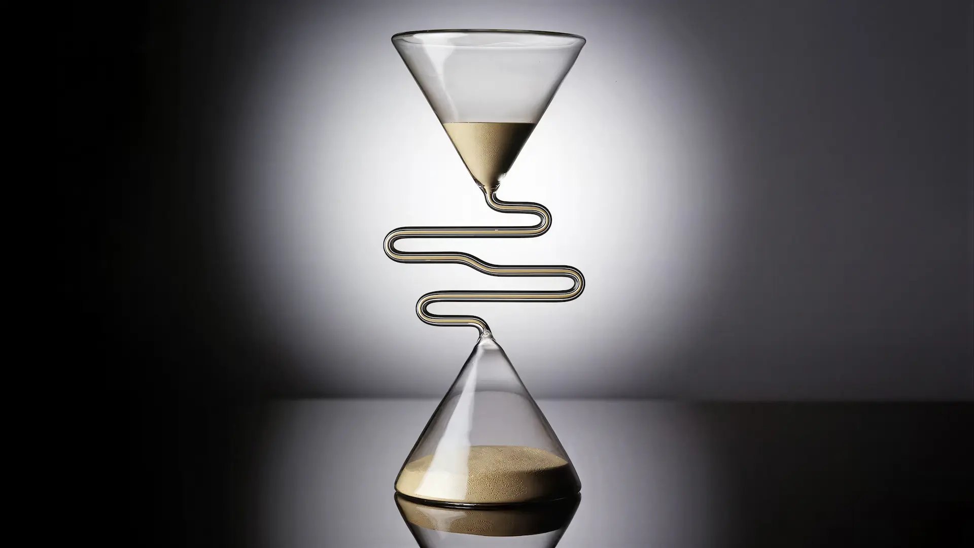 Hourglass with a serpentine path between its two glass chambers, dimly lit on a dark surface.