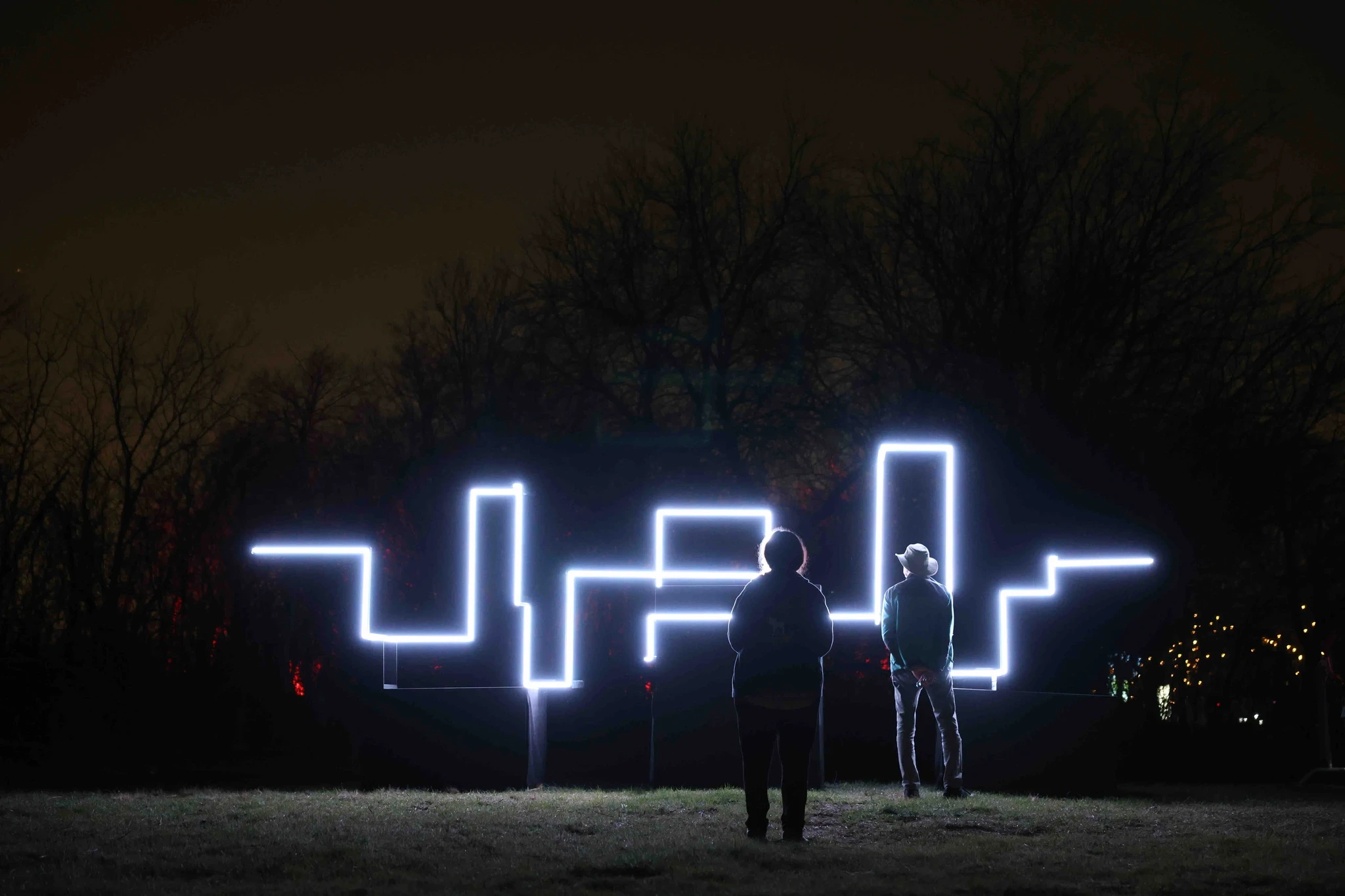 A dark scene featuring illuminated abstract shapes or patterns created by lights against a night sky.