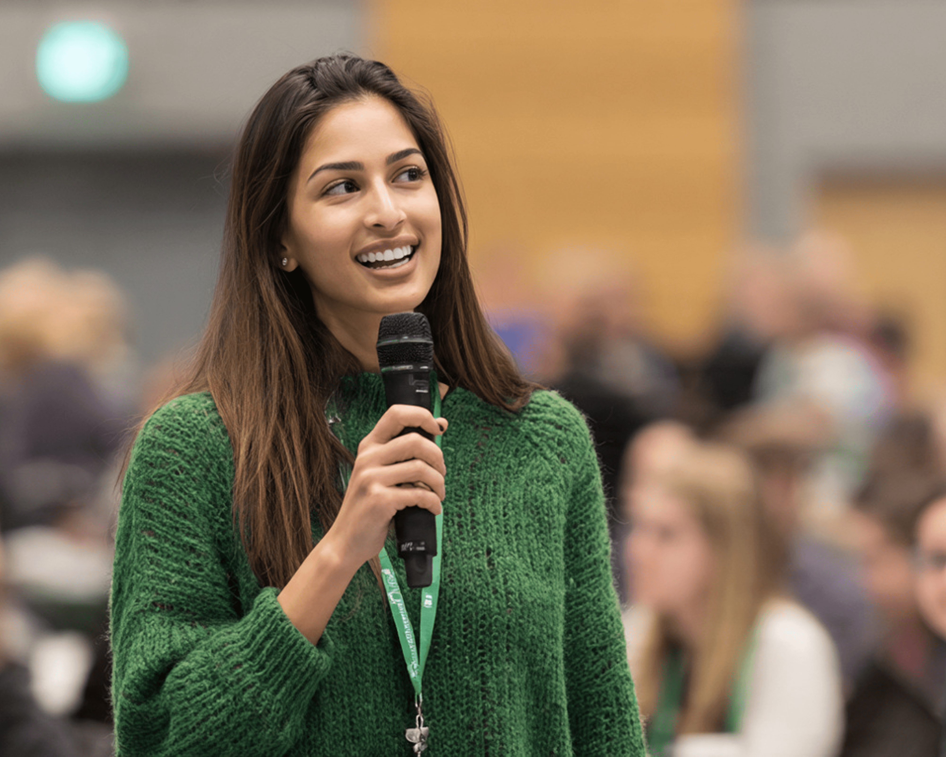 Person in green sweater speaking with microphone at event