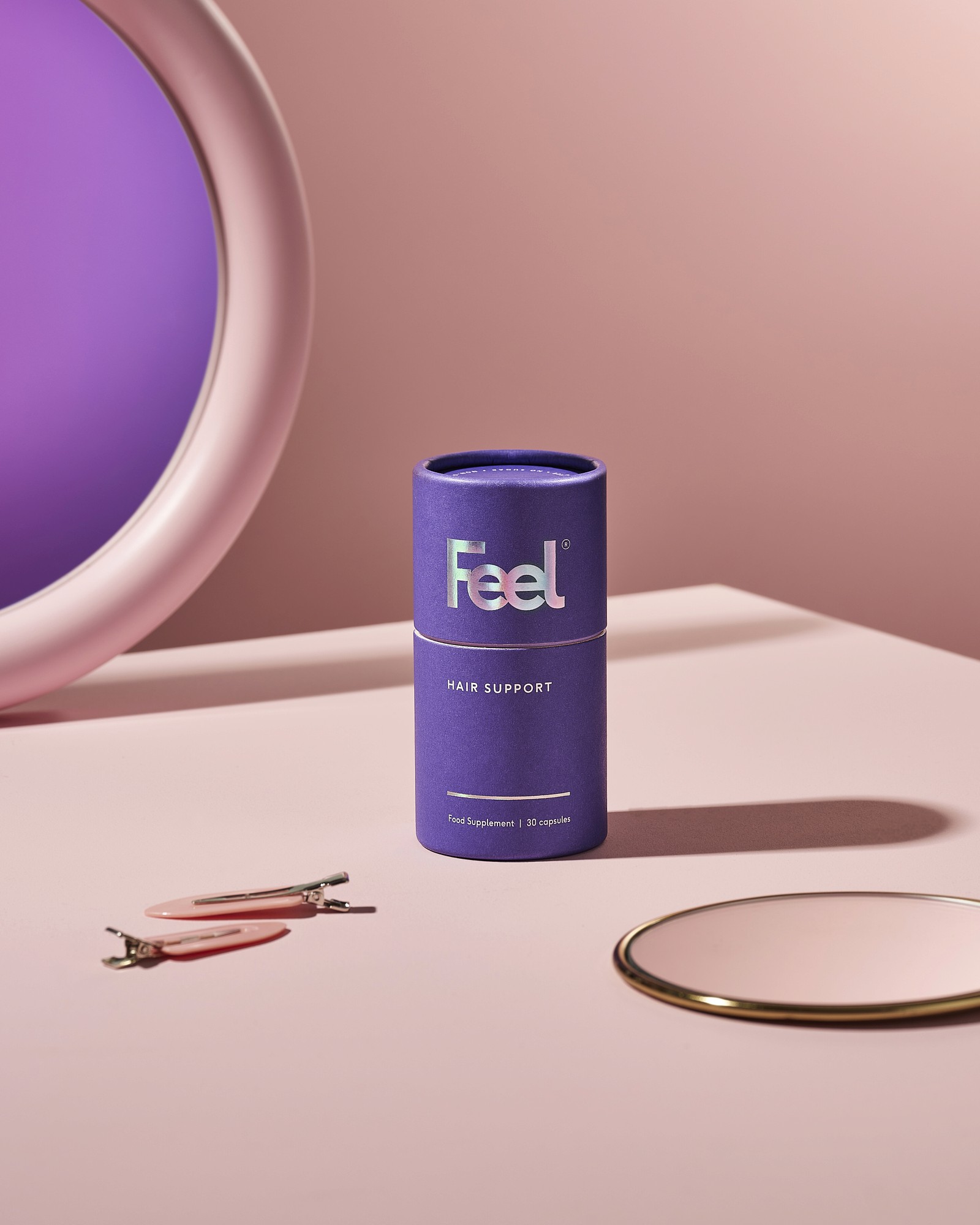 A purple cylindrical container on a pale surface, next to a round mirror and a small circular object.