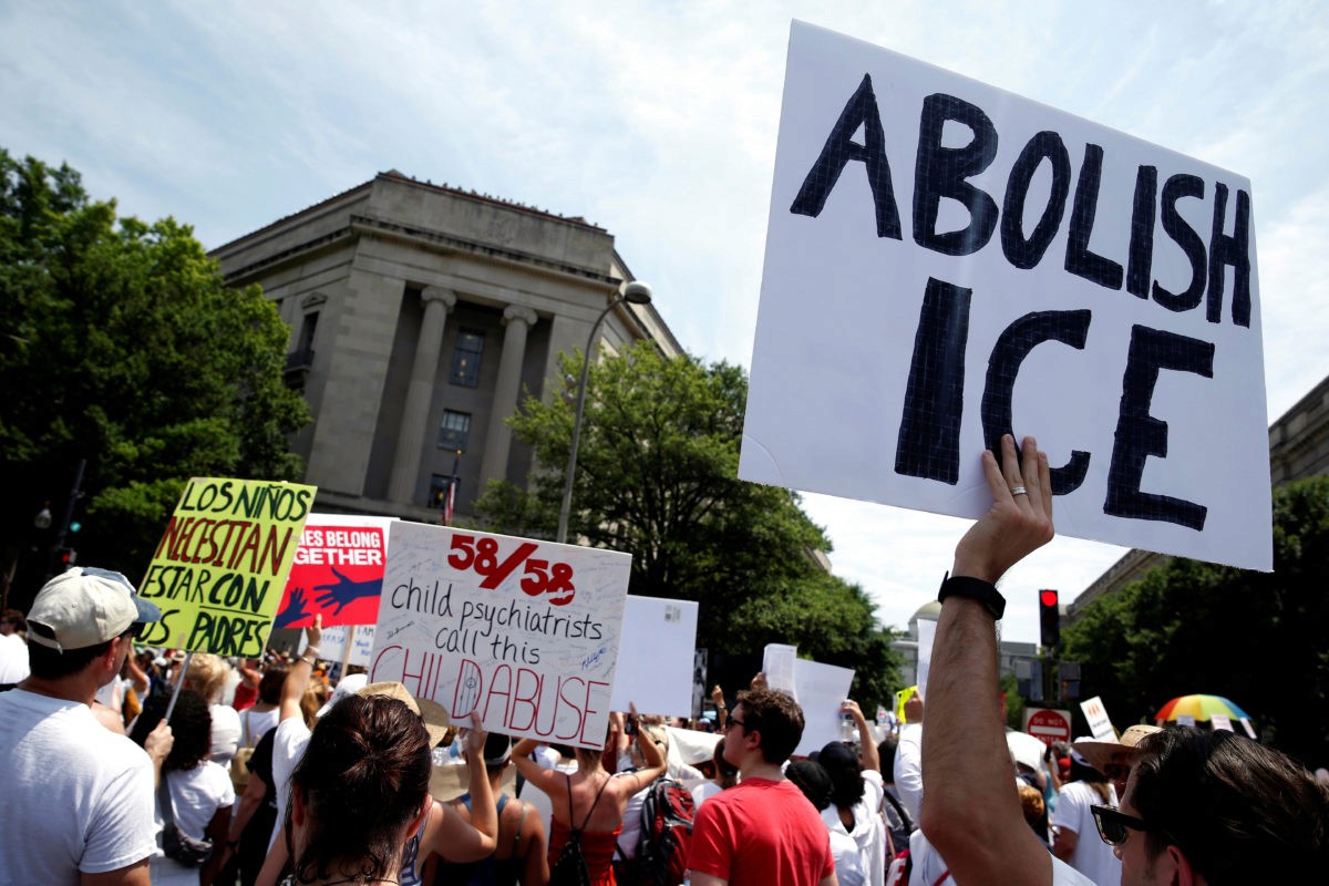 A large group of protestors gathers outside a government building holding signs with messages including "Abolish ICE" and "Child psychiatrists call this child abuse," expressing strong opposition to immigration policies.