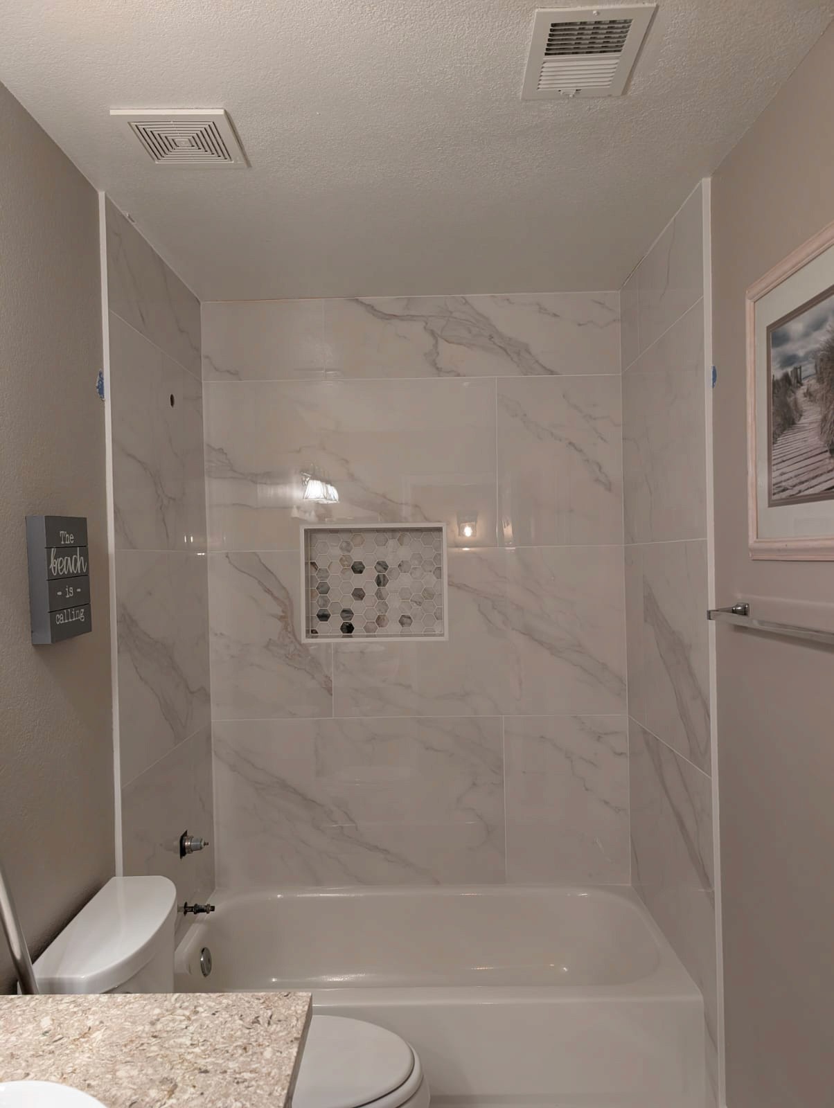Elegant bathroom tub and shower surround with large format white marble-look wall tiles, featuring a contrasting mosaic tile shower niche.