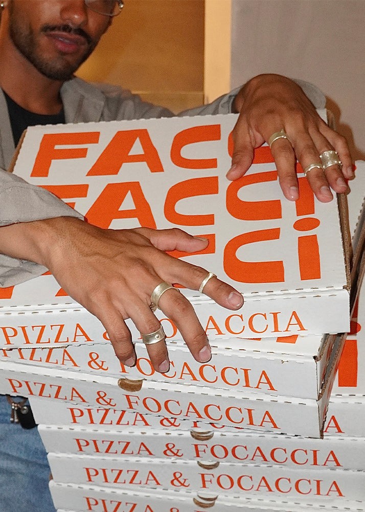 Person wearing multiple silver rings holding a stack of pizza boxes from Facci restaurant.