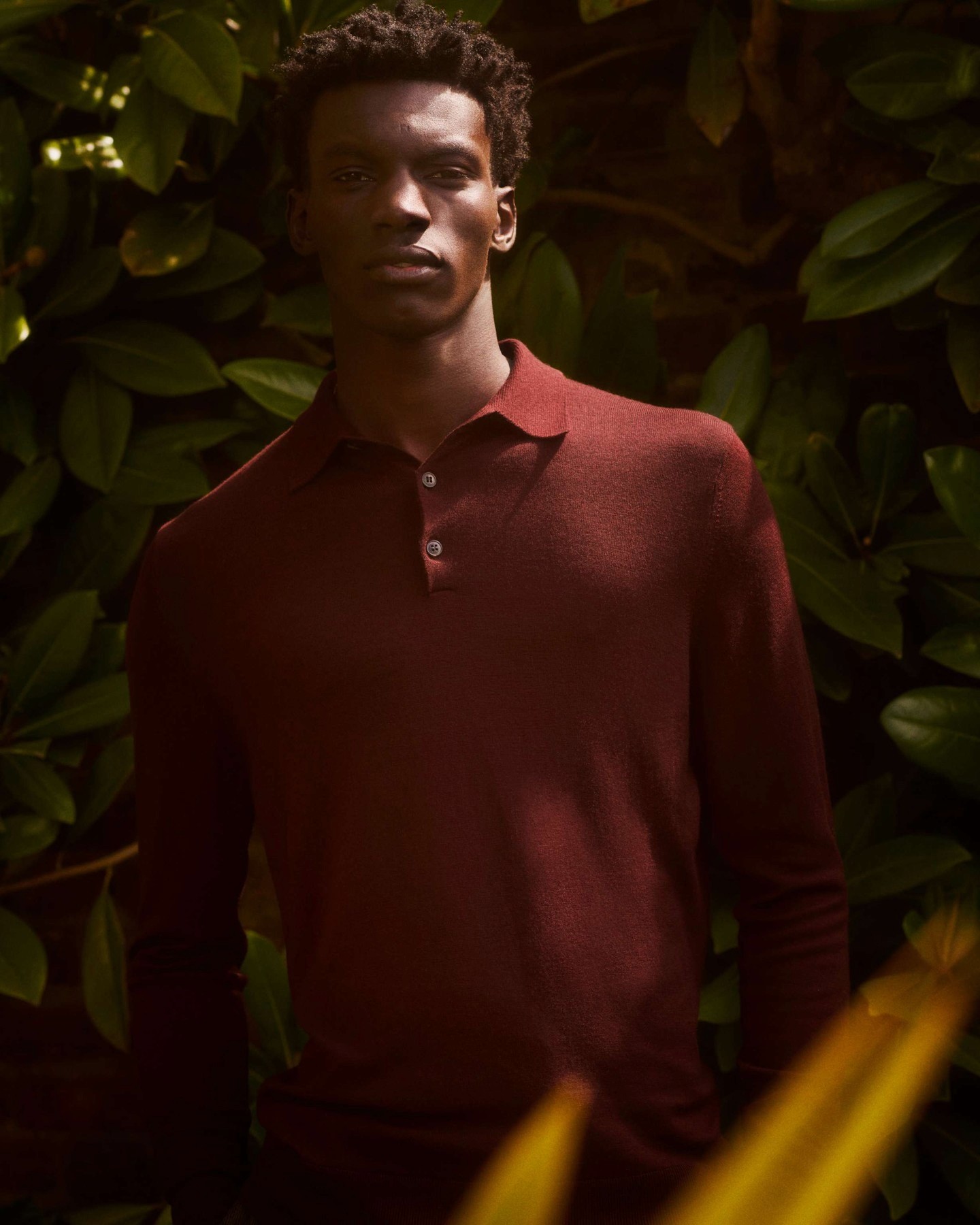 Dans le lookbook Sunspel, un homme porte un polo rouge dans un jardin