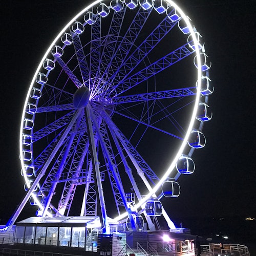 在夜晚，亮燈的摩天輪有著封閉的艙，閃爍著藍色和白色的燈光。