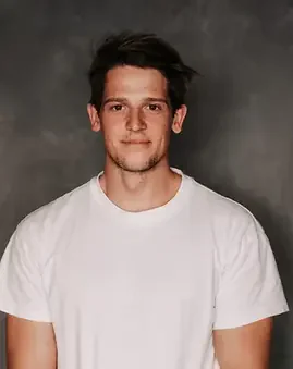 Markus Schmoltner im weißen T-Shirt blickt vor grauem Hintergrund in die Kamera