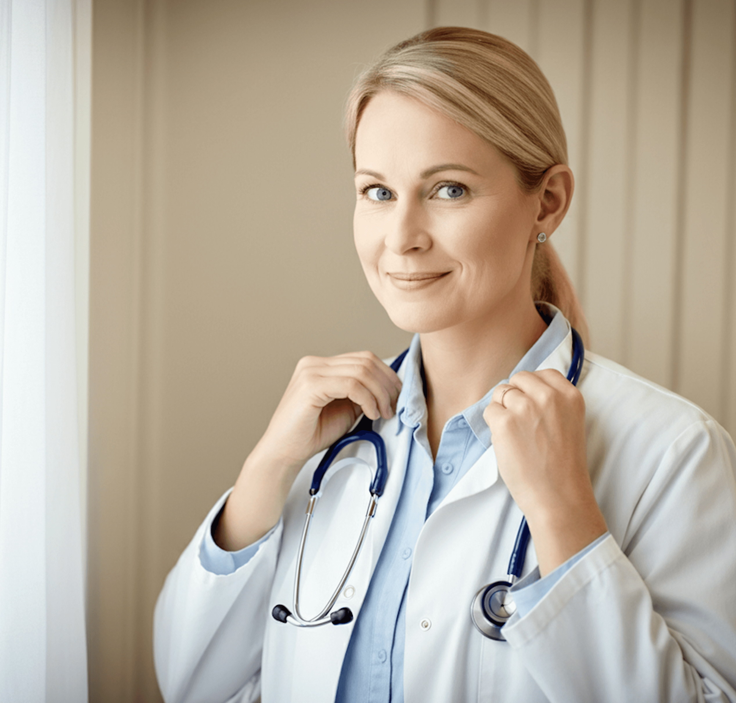 Doctor in white coat holding stethoscope near window with vertical blinds, light hair pulled back.