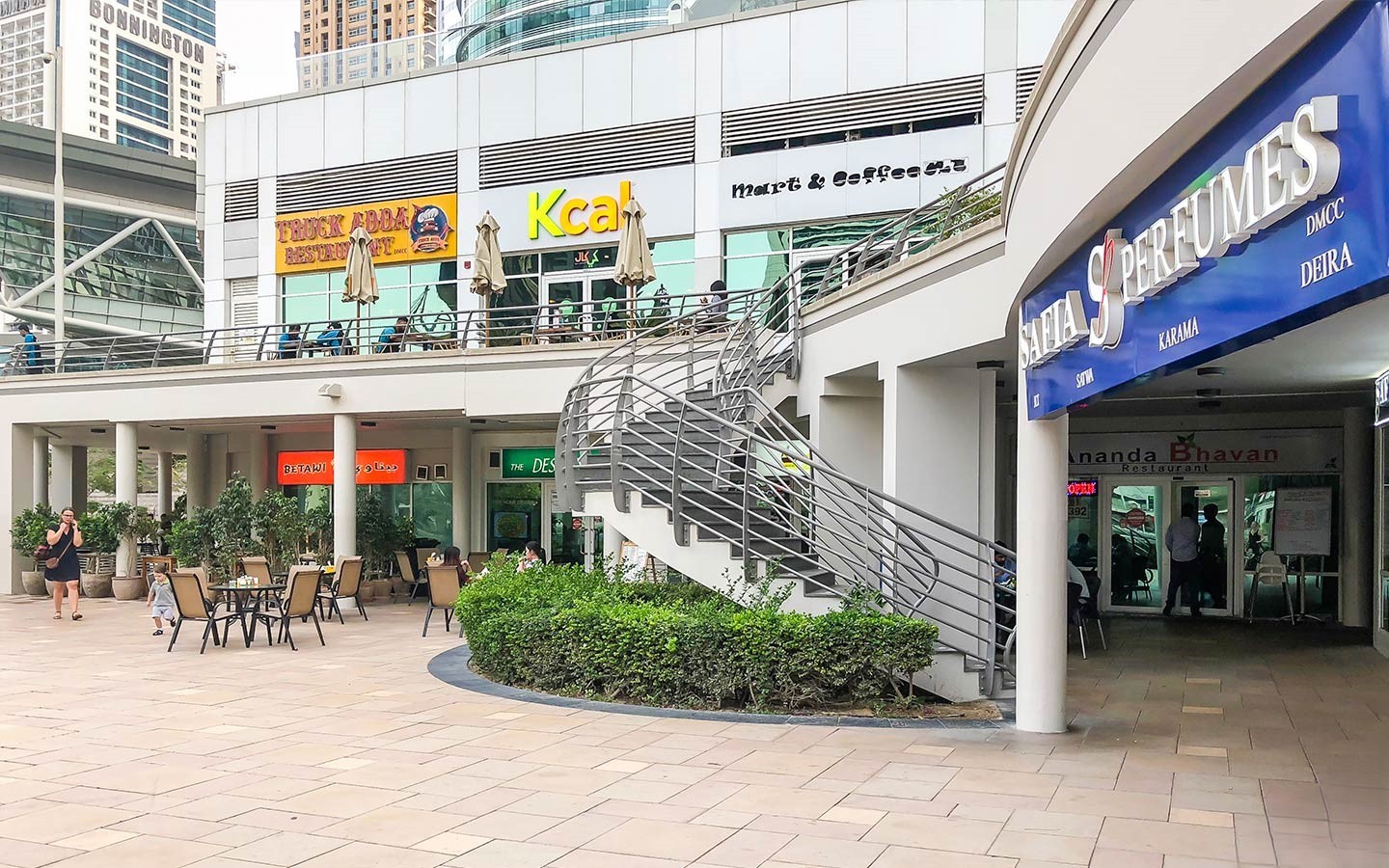An outdoor area with a spiral staircase leading to shops like Kcal and Mart & Coffee Co. in the Jumeirah Lake Towers complex.