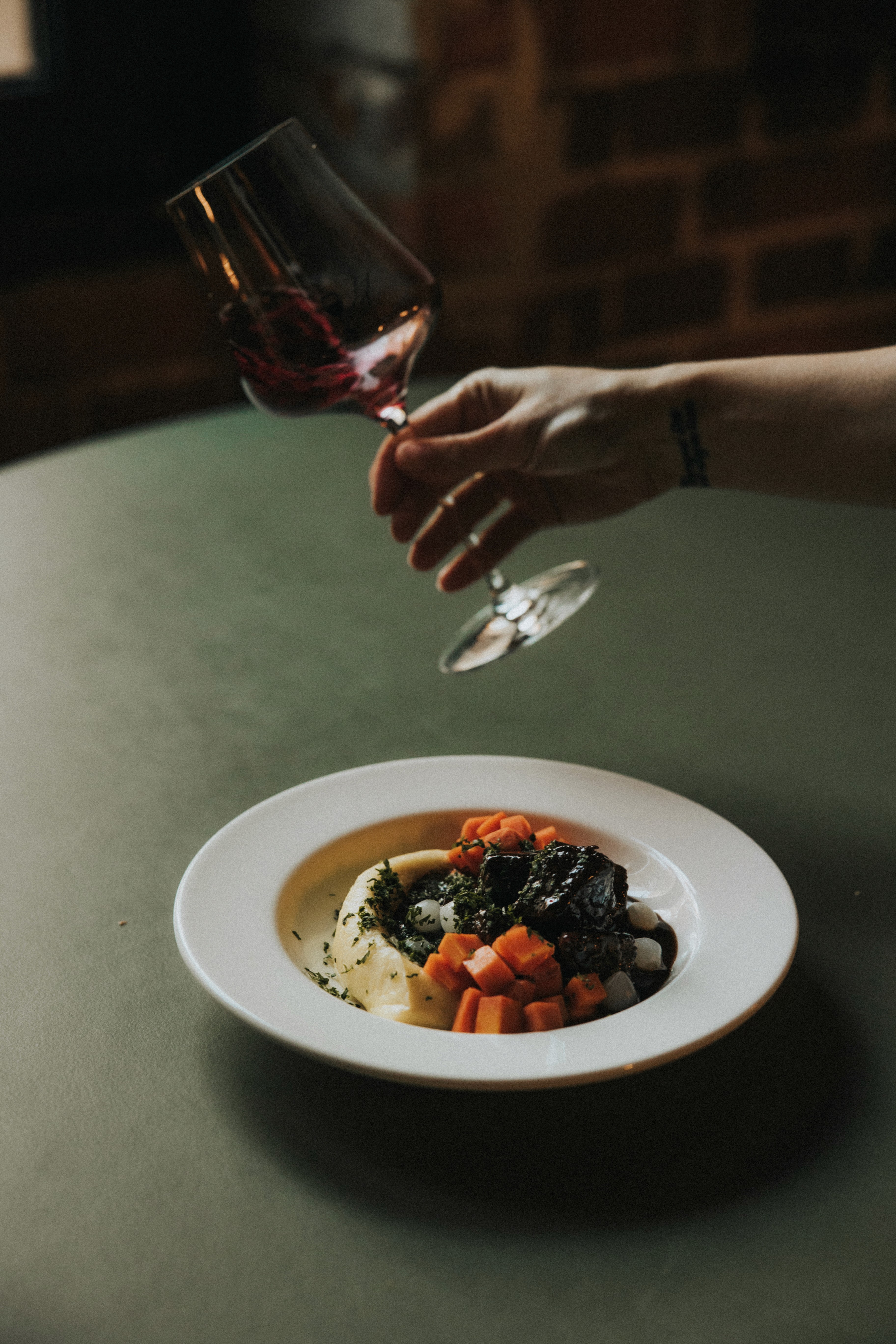 Ręka trzymająca butelkę znajduje się na ciemnym tle, rzucając cień na powierzchnię powyżej.