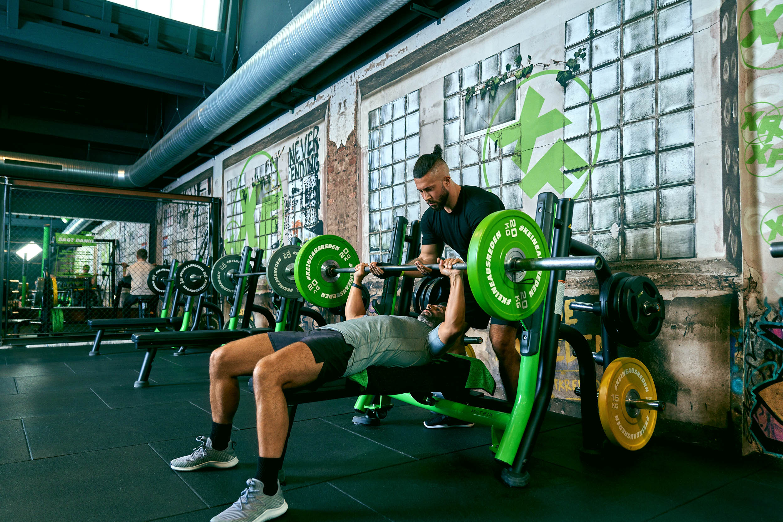  Zwei XTRAFIT-Mitglieder beim Bankdrücken im XTRAFIT Fitnessstudio, trainieren Kraft und Kognition mit gezieltem Gewichtheben.