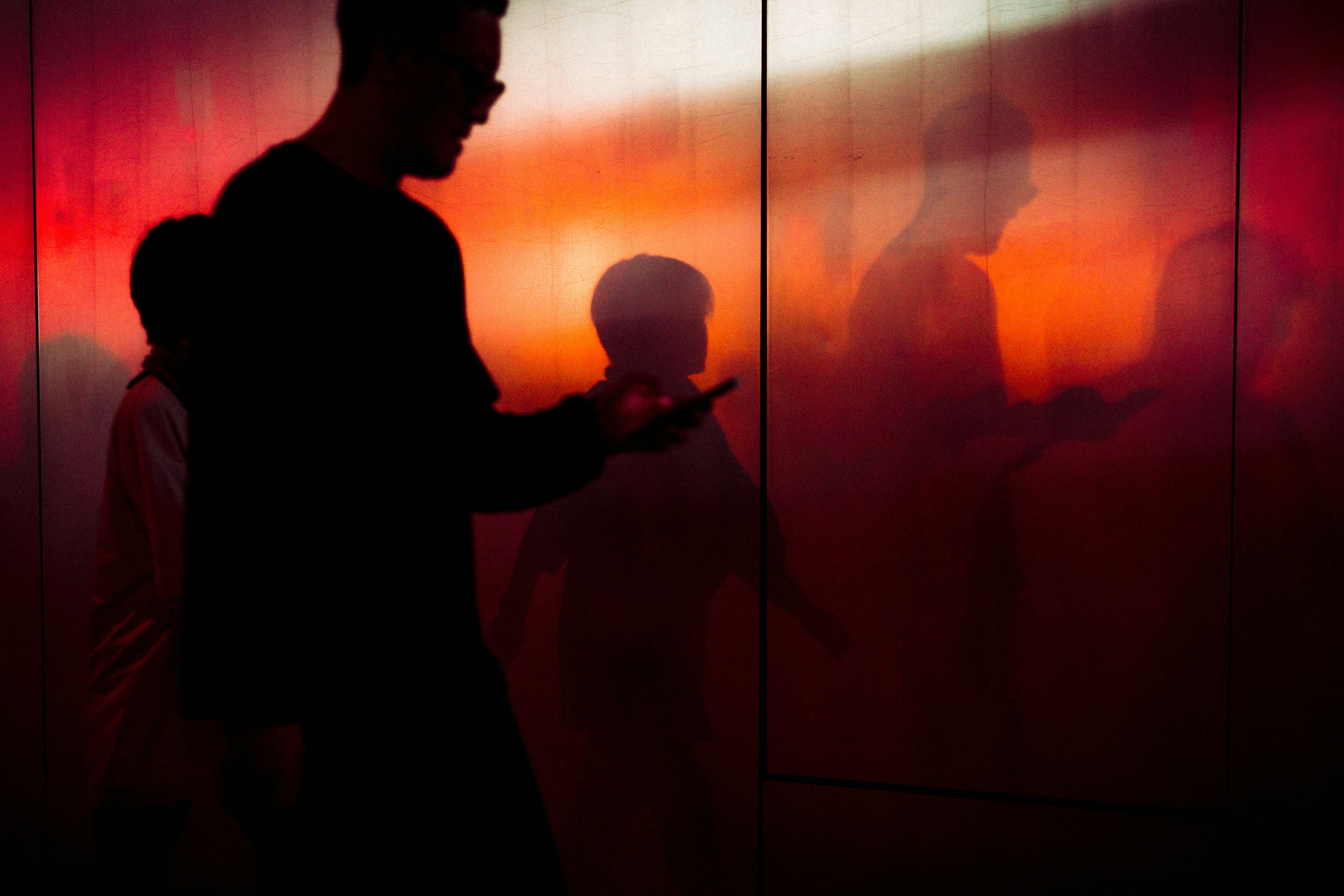Silhouetted people stand in a red lit area.