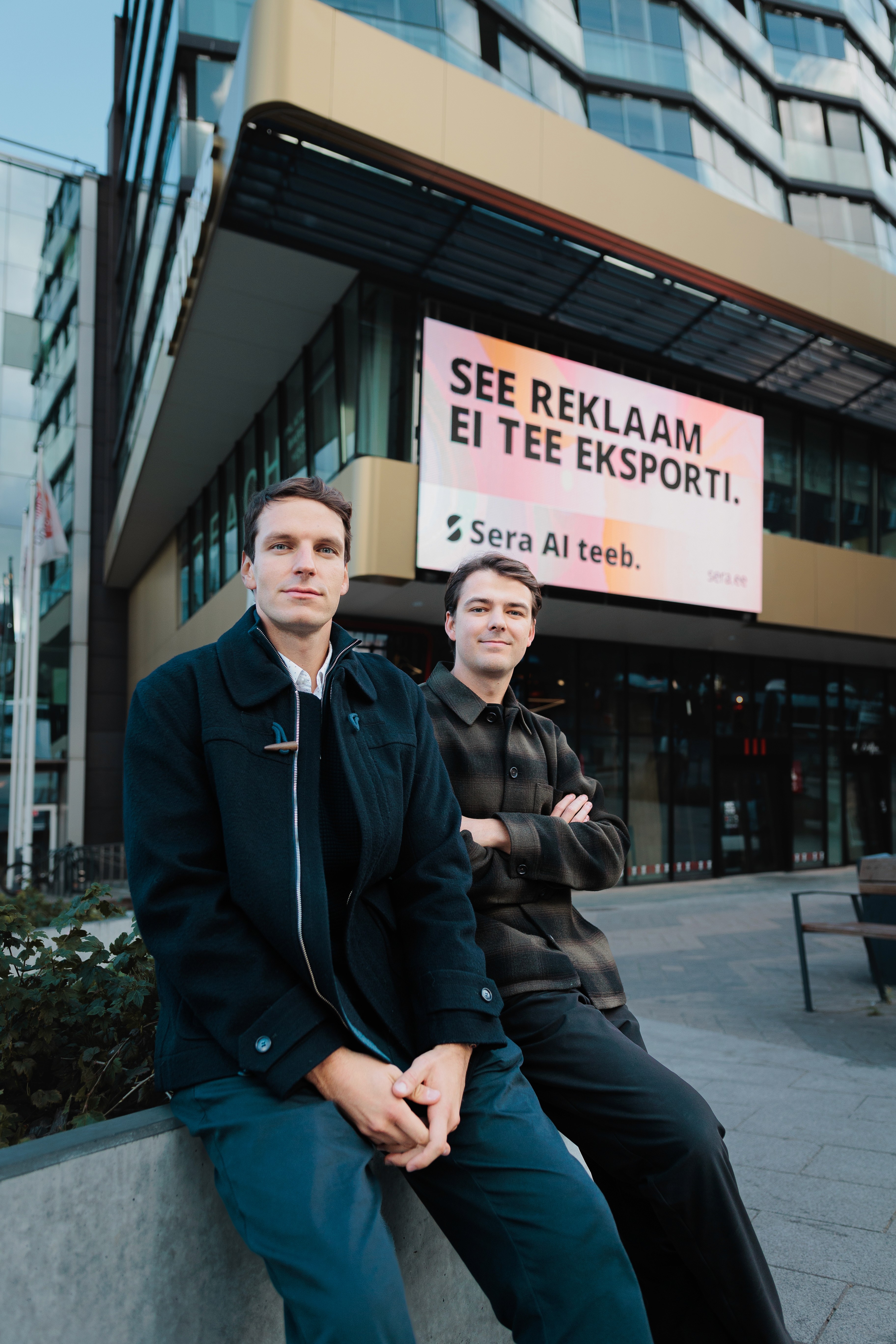 Three people sit around a high black table in a dimly lit room, each engrossed in their smartphones, reading spam mail probably, with coffee cups in front of them.