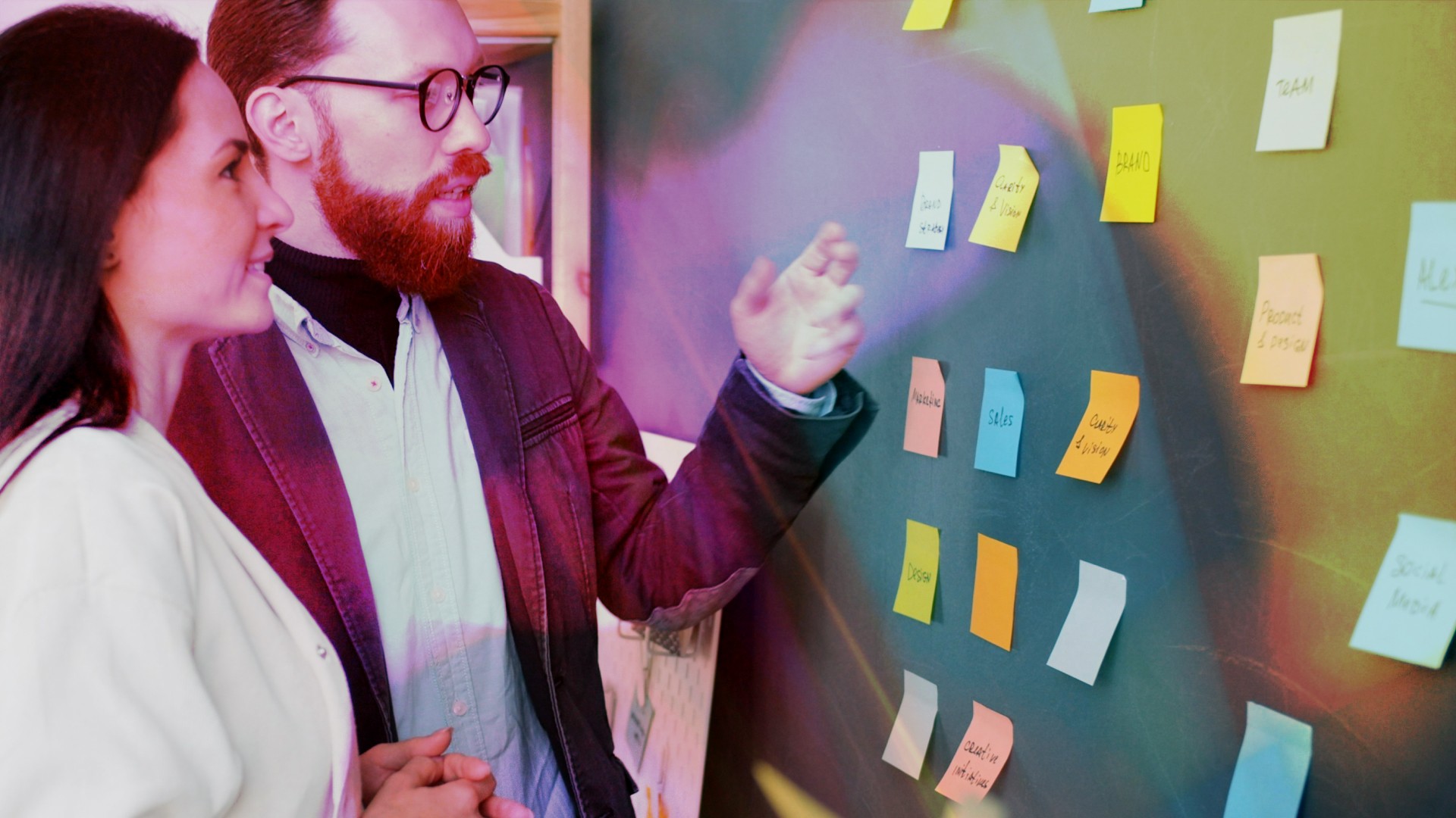 Two people looking at a blackboard covered in sticky notes