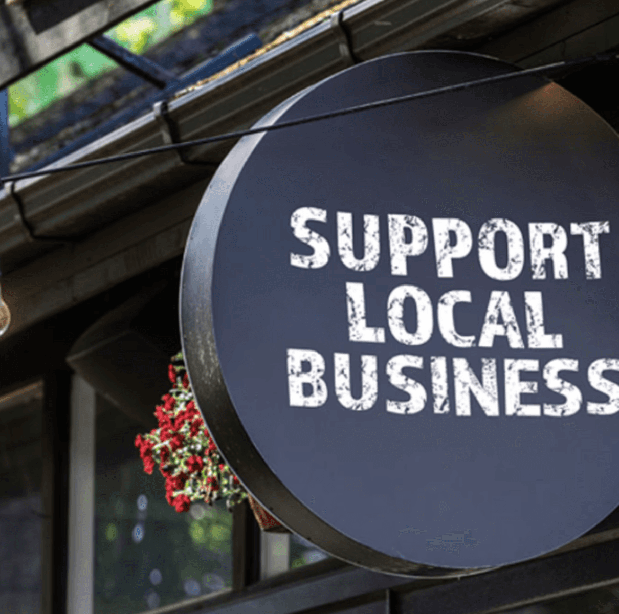 A smiling man with curly hair is sitting at a desk, looking at the camera, with a laptop and a lamp in the background.