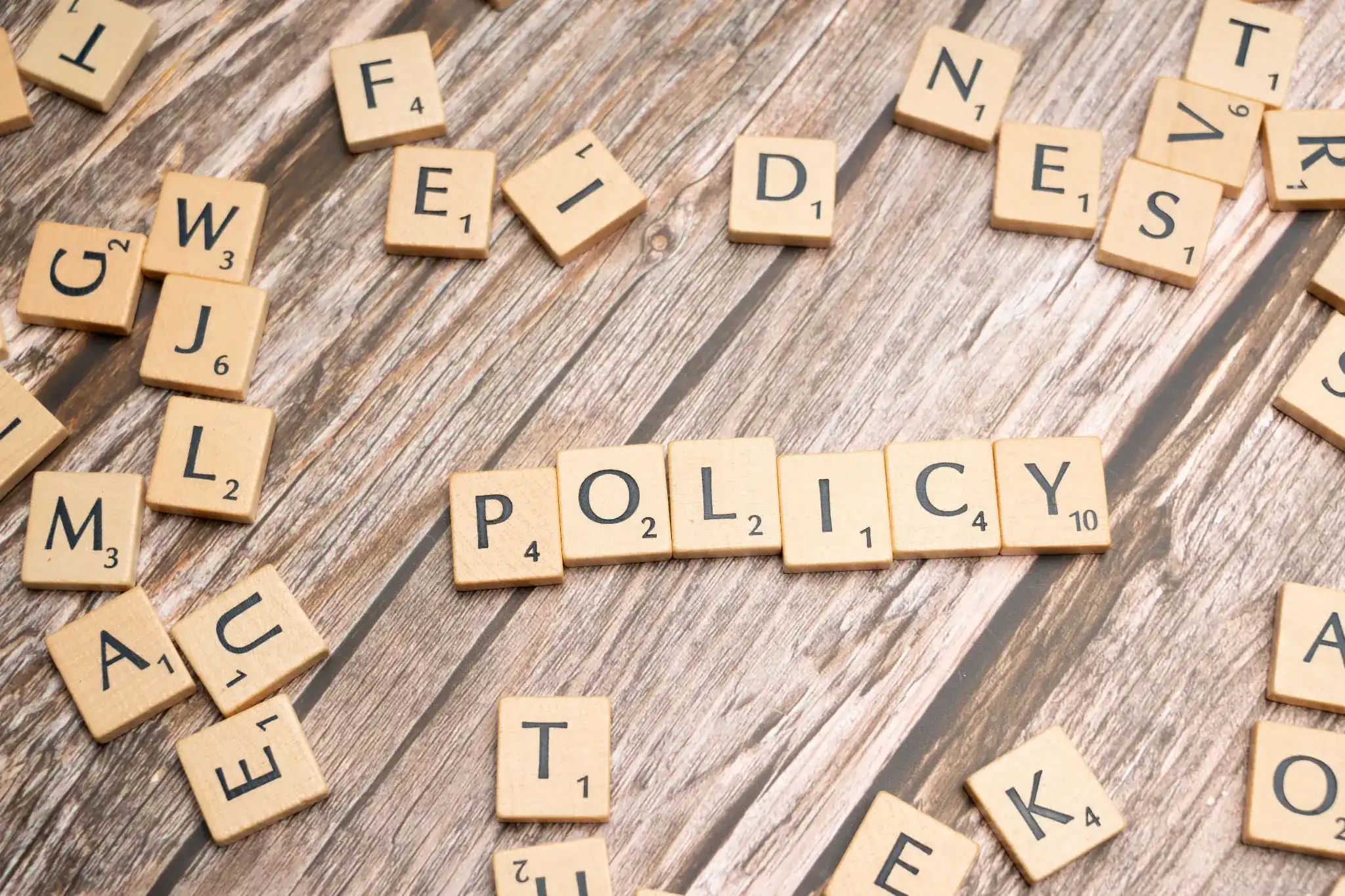 Wooden letter tiles spelling “POLICY” on a rustic desk, representing business policy, compliance, governance, and professional standards.