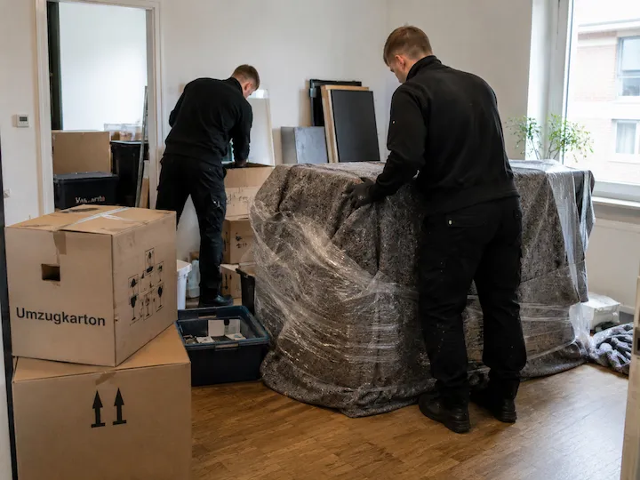 Zwei Mitarbeiter verpacken Möbel und Umzugskartons in einer Wohnung