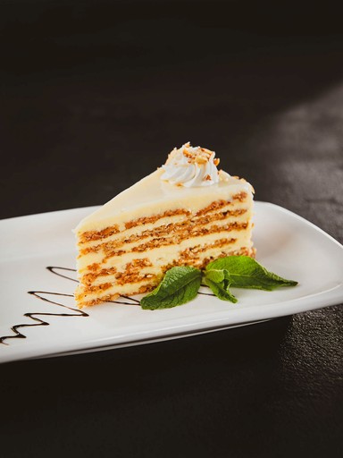 A slice of layered cake with white frosting and a sprig of mint on a white plate.