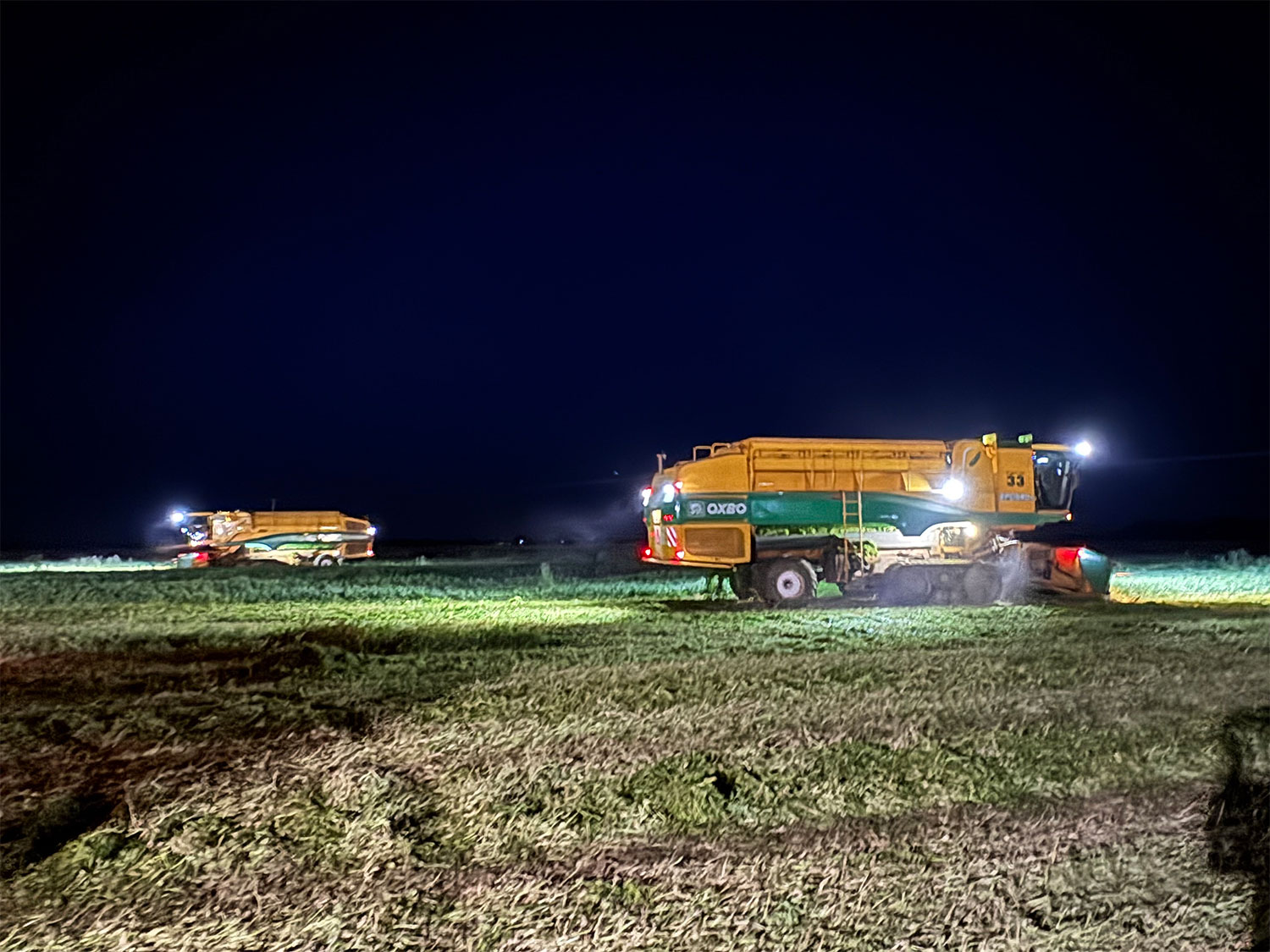 Two Ploeger pea harvesters using their lights whilst harvesting against a night sky